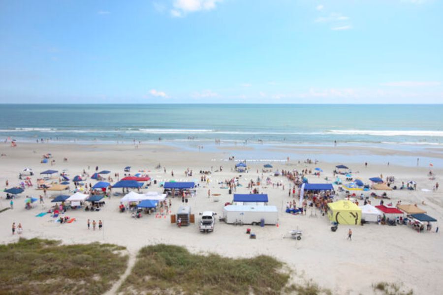 Aerial view of a crowded Surfers for Autism beach event with tents and participants along the shoreline