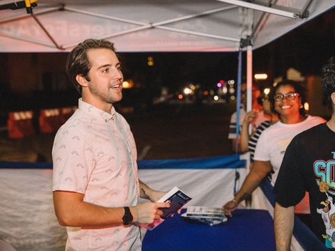 Cash Lambert smiling while holding a book and flyer at a nighttime outdoor booth