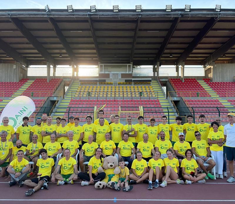 Foto di gruppo di atleti e allenatori dei Daini in maglia gialla, sulla pista davanti alle tribune