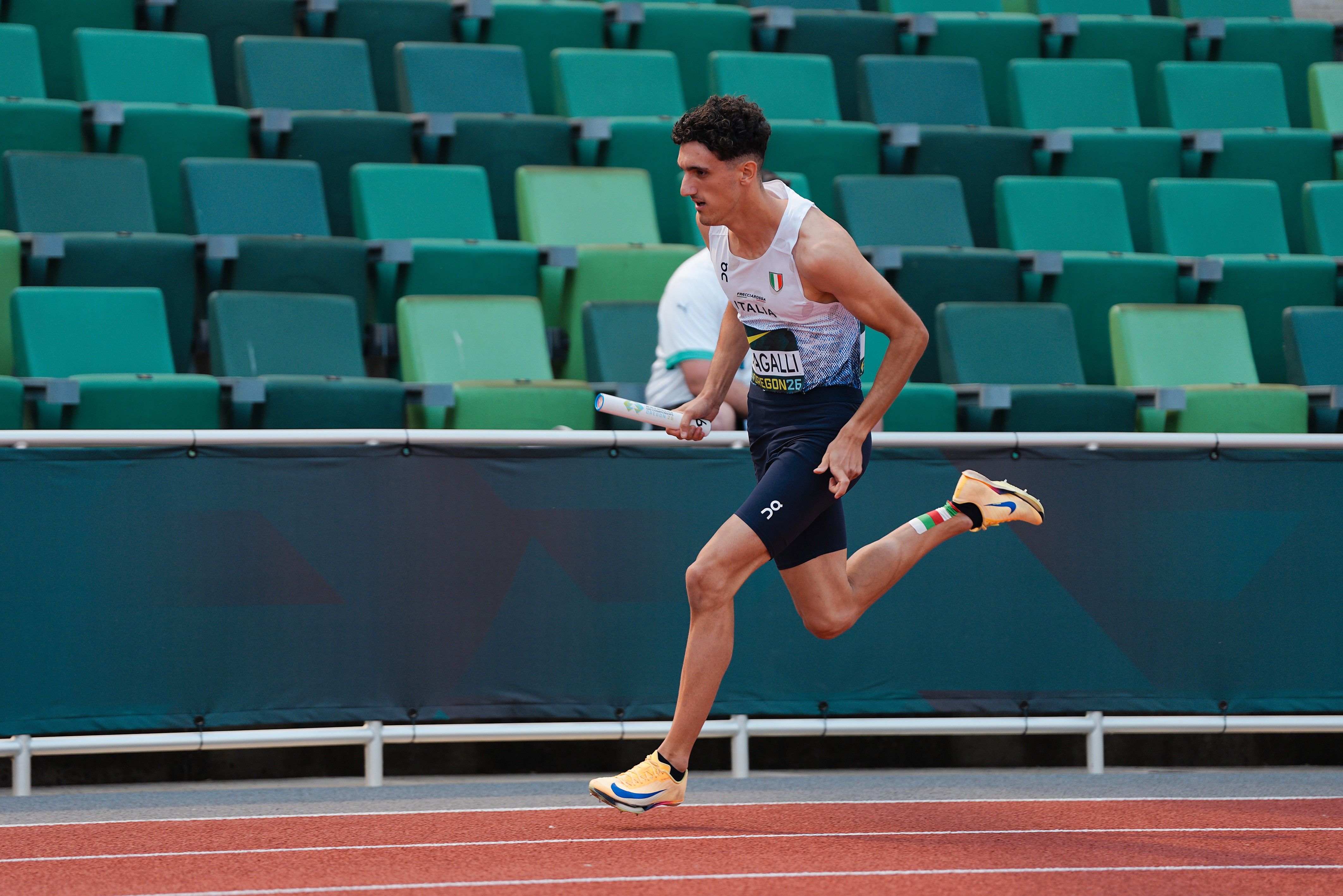 Un atleta con il testimone corre in pista davanti alle tribune verdi