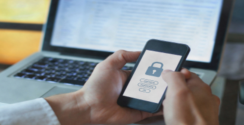 Man holding a phone that has a screenshot of a lock working in front of a laptop