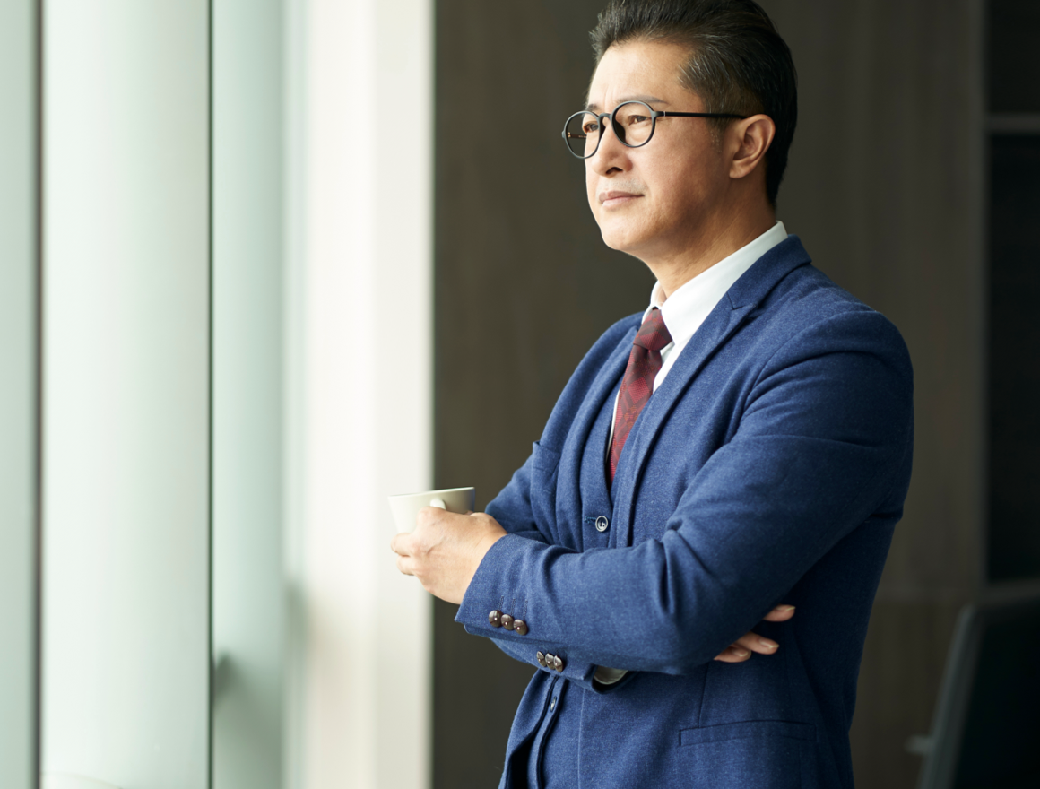 Businessman in deep thought looking out the window holding a mug of tea or coffee