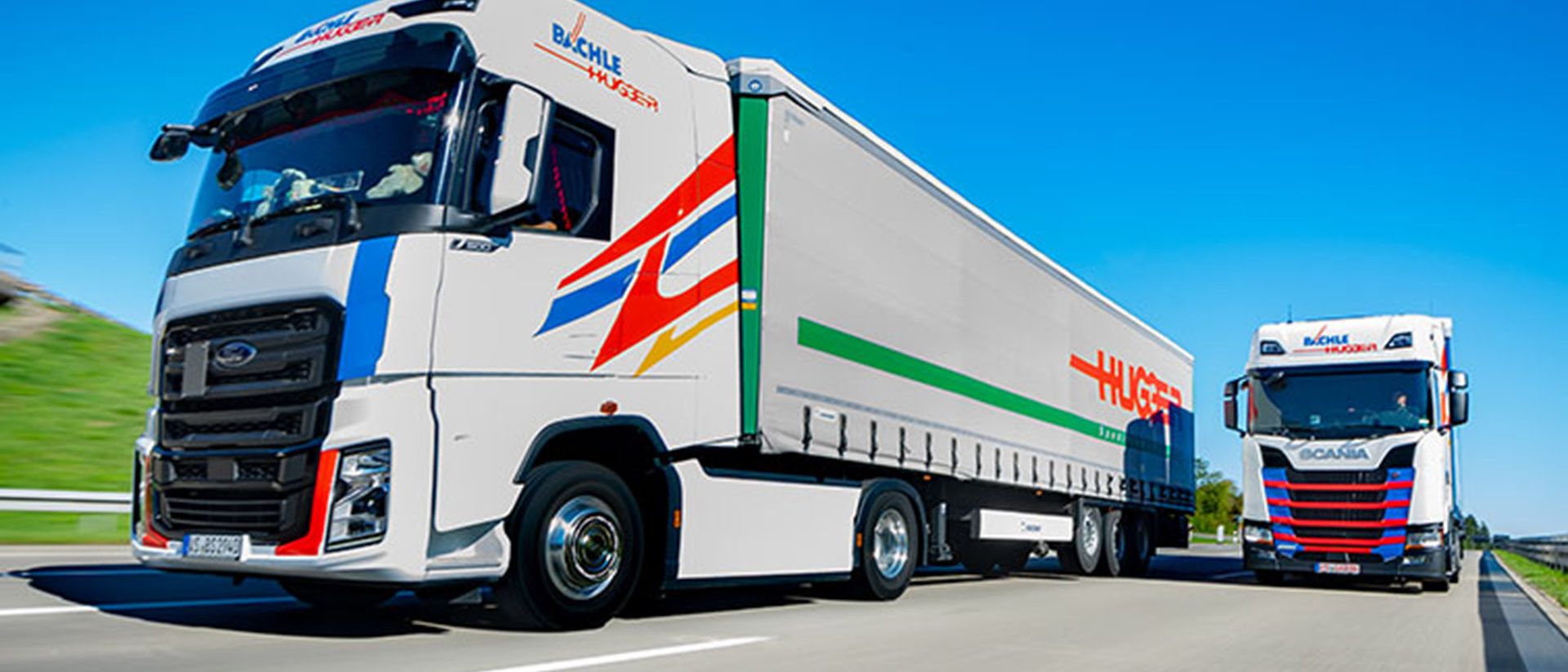 Ein Swiss Post Cargo LKW und ein Bächle LKW stehen nebeneinander.