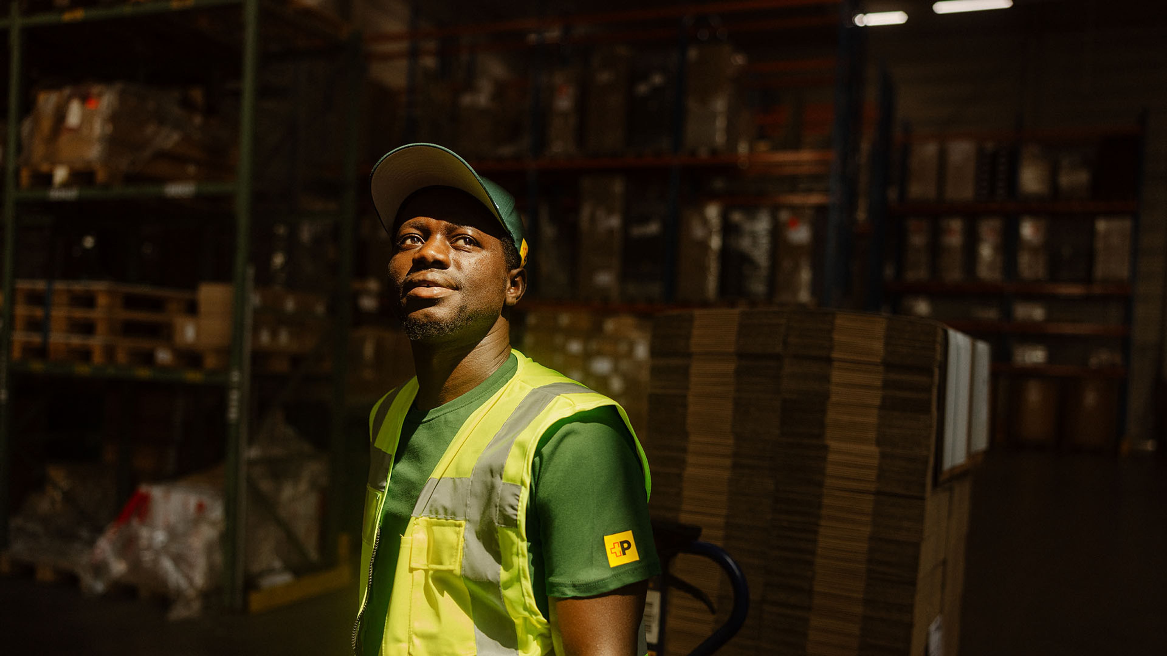 Swiss Post Cargo employee in high visibility vest stands in front of storage room with parcels.