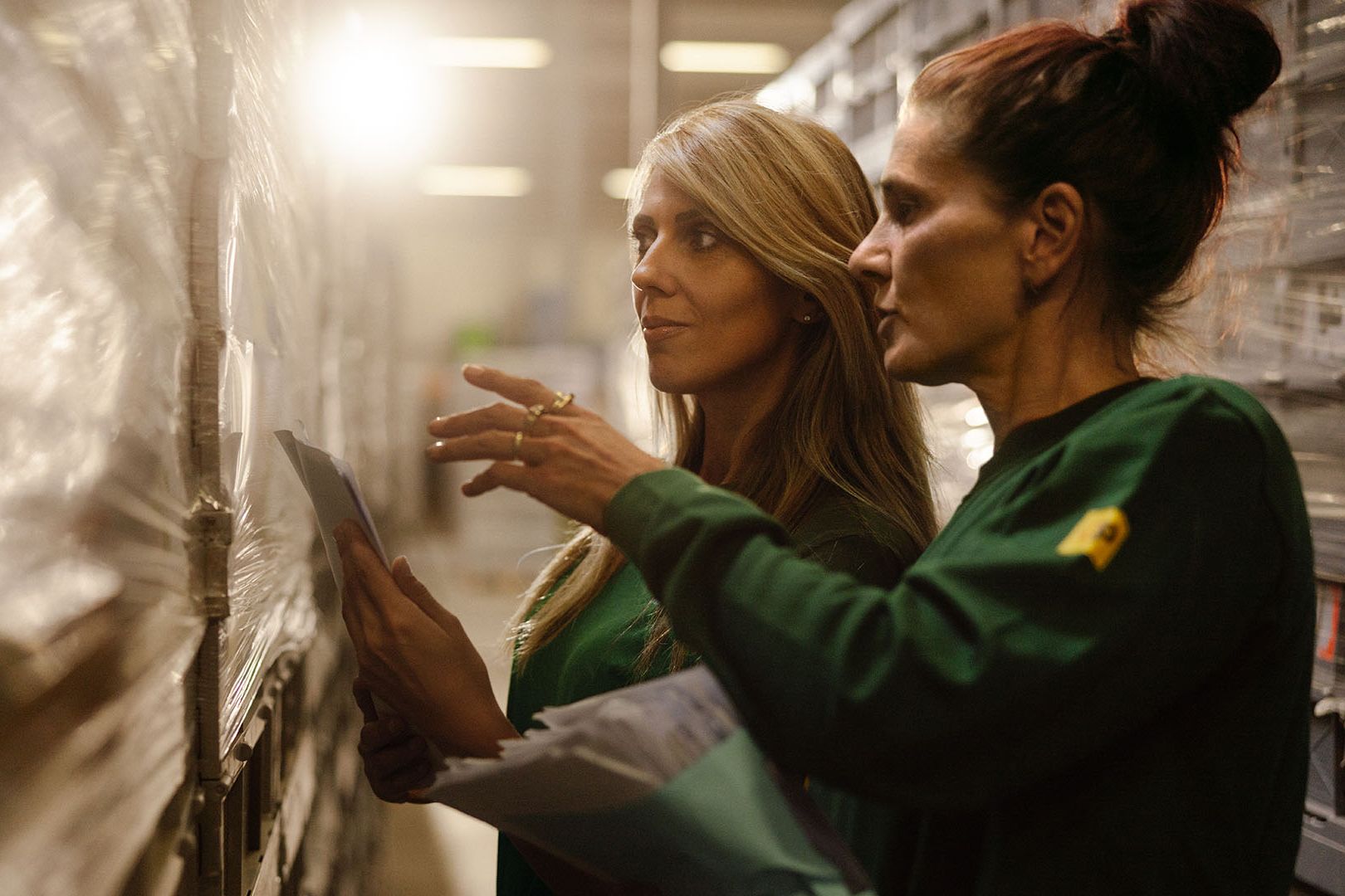 Two Swiss Post Cargo employees stand in front of a storage shelf.