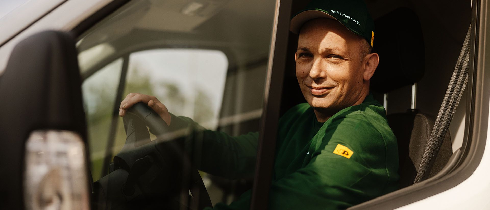 Un chauffeur de Swiss Post Cargo conduit un véhicule de livraison avec des envois de courrier de jour.