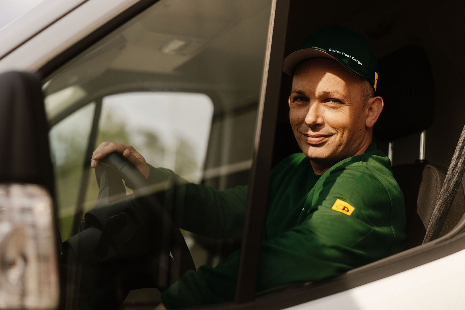 Un chauffeur de Swiss Post Cargo conduit un véhicule de livraison avec des envois de courrier de jour.