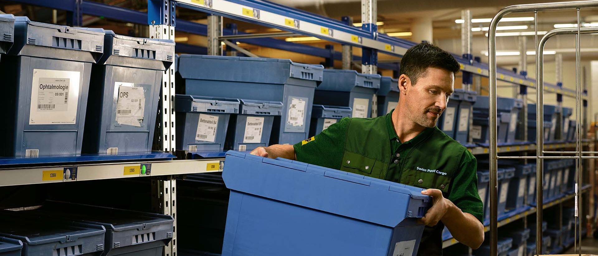 Un employé d'entrepôt charge une boîte de produits pharmaceutiques d'une étagère sur un chariot.