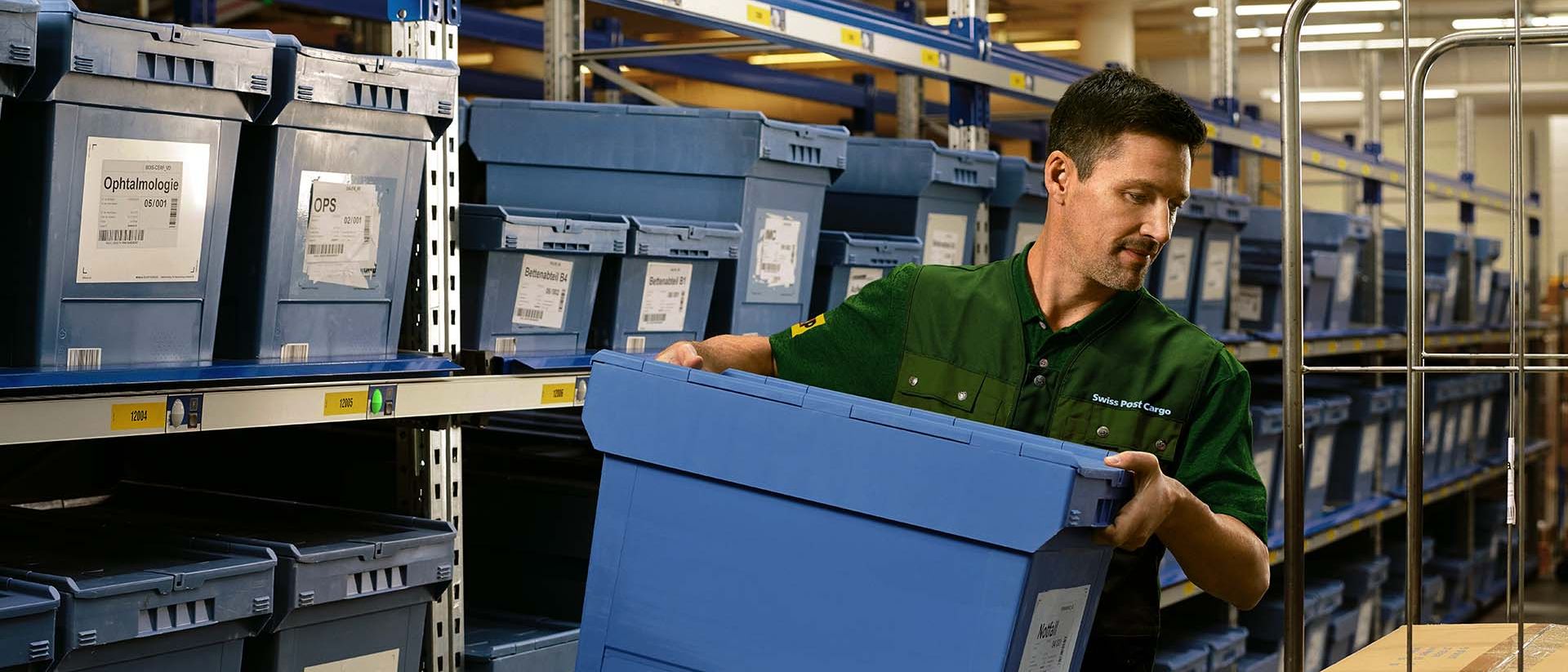 Un employé d'entrepôt charge une boîte de produits pharmaceutiques d'une étagère sur un chariot.