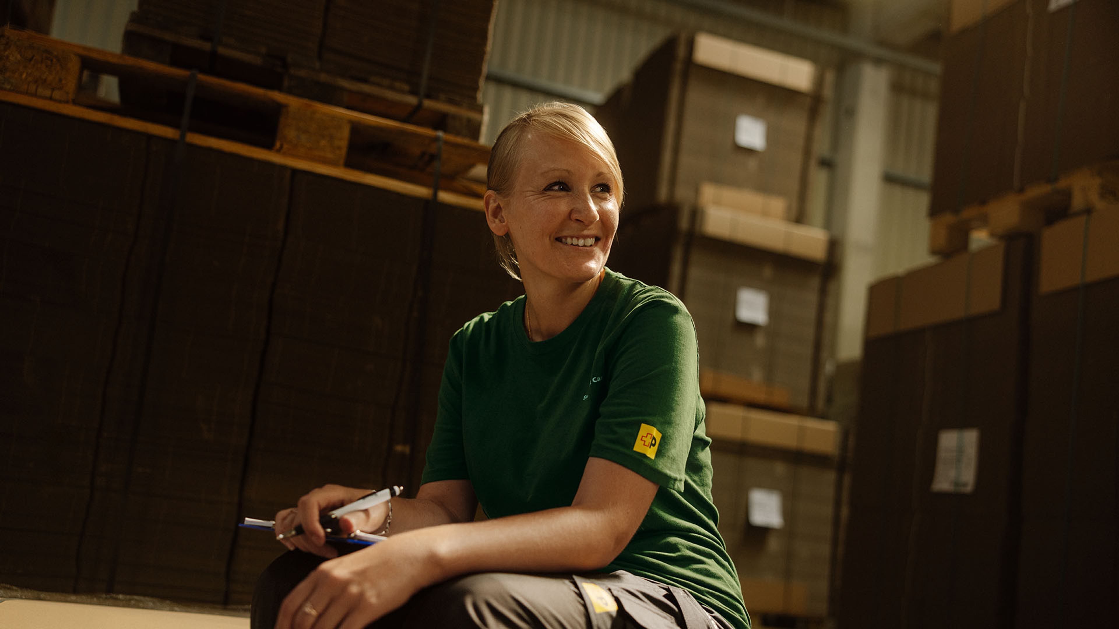 A smiling Swiss Post Cargo employee in front of the shelf in the storage room.