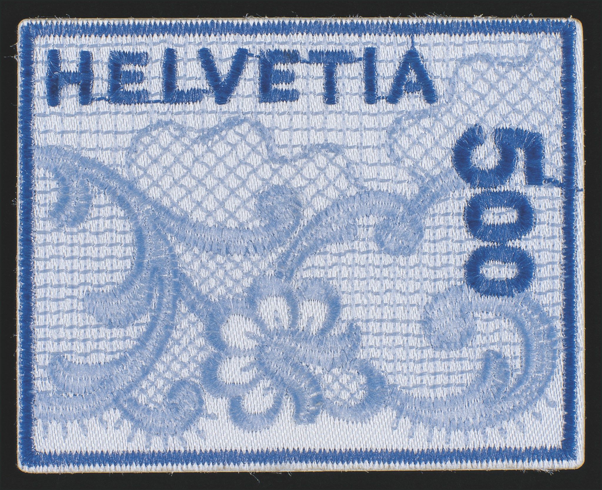 Schweizer Briefmarke in Stickerei-Optik, hellblau mit dunkelblauen Details. Florales Muster und die Aufschrift ‚Helvetia‘ oben sowie ‚500‘ senkrecht rechts.