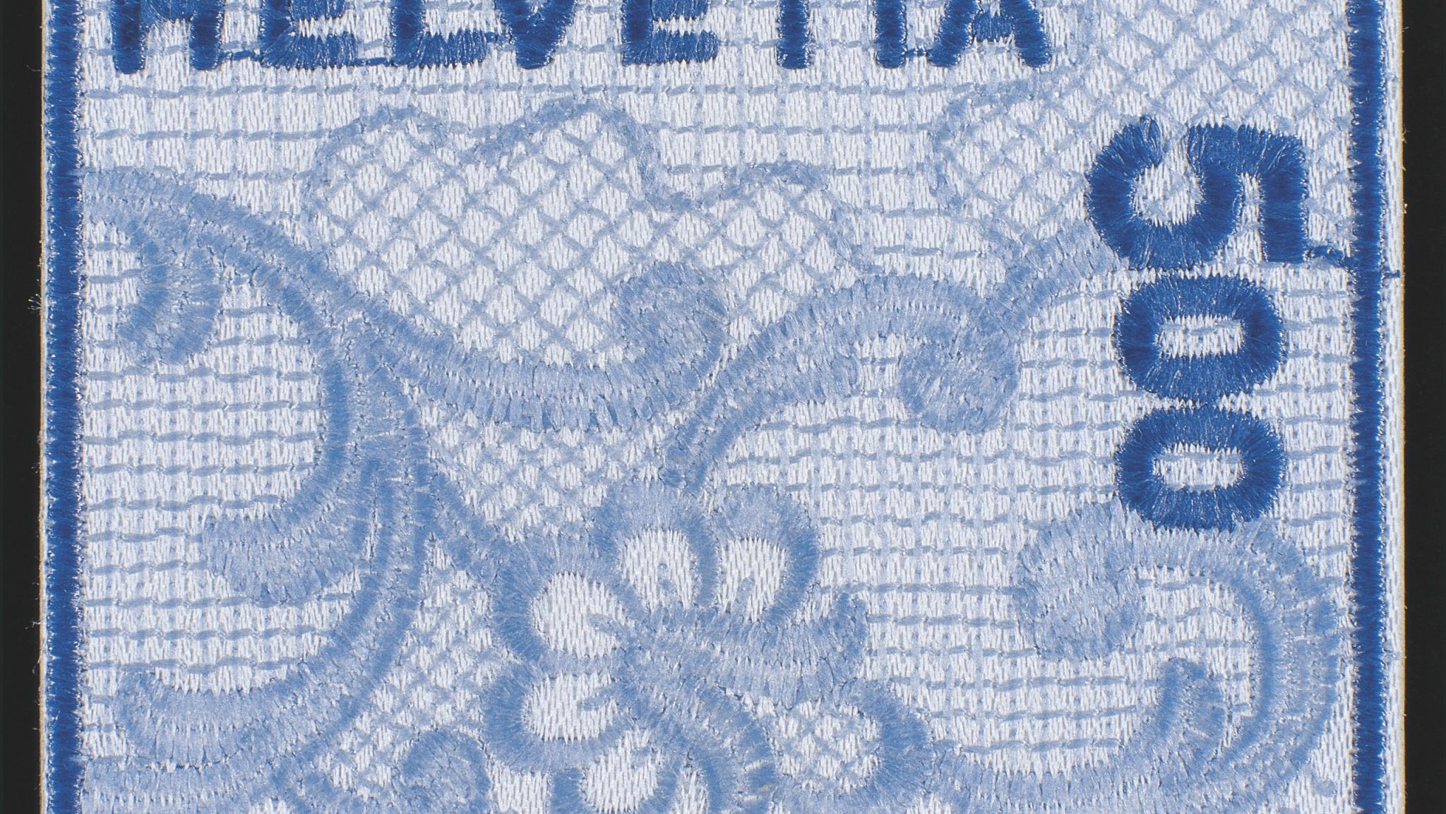 Schweizer Briefmarke in Stickerei-Optik, hellblau mit dunkelblauen Details. Florales Muster und die Aufschrift ‚Helvetia‘ oben sowie ‚500‘ senkrecht rechts.