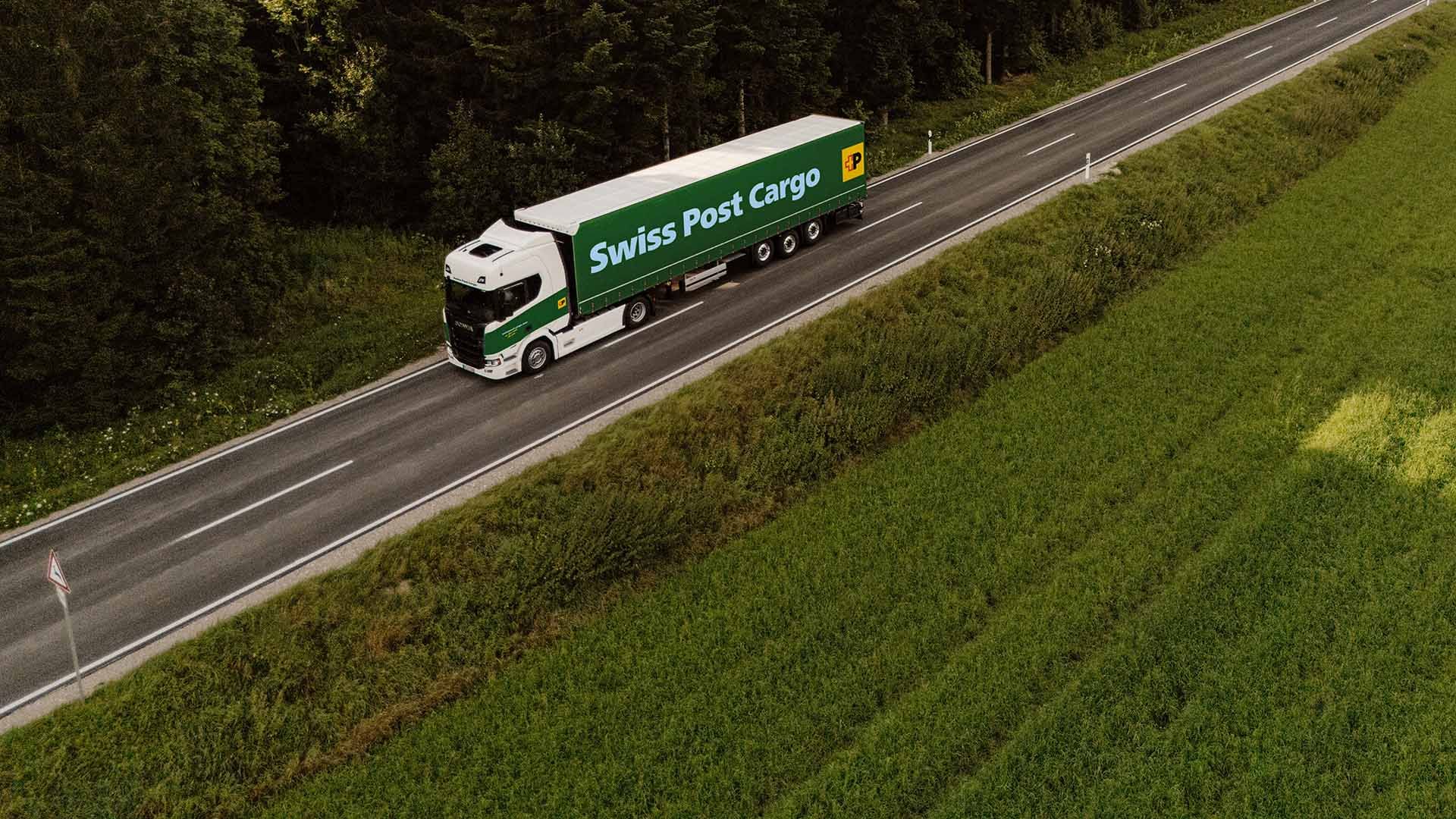 Un camion Swiss Post Cargo roule sur une route nationale à la lisière de la forêt