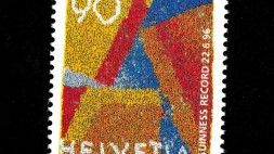 Schweizer Briefmarke mit farbigem abstraktem Muster in Gelb, Rot und Blau. Aufschrift: ‚90‘, ‚Helvetia‘ und ‚Guinness Record 22.6.96‘.