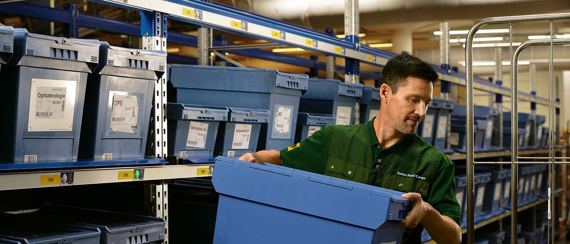 Ein Lagermitarbeiter lädt eine Box mit Pharma-Waren von einem Regal auf einen Rollwagen.