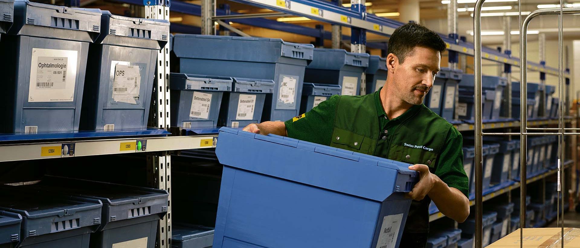 A warehouse worker loads a box with pharmaceutical goods from a shelf onto a trolley.