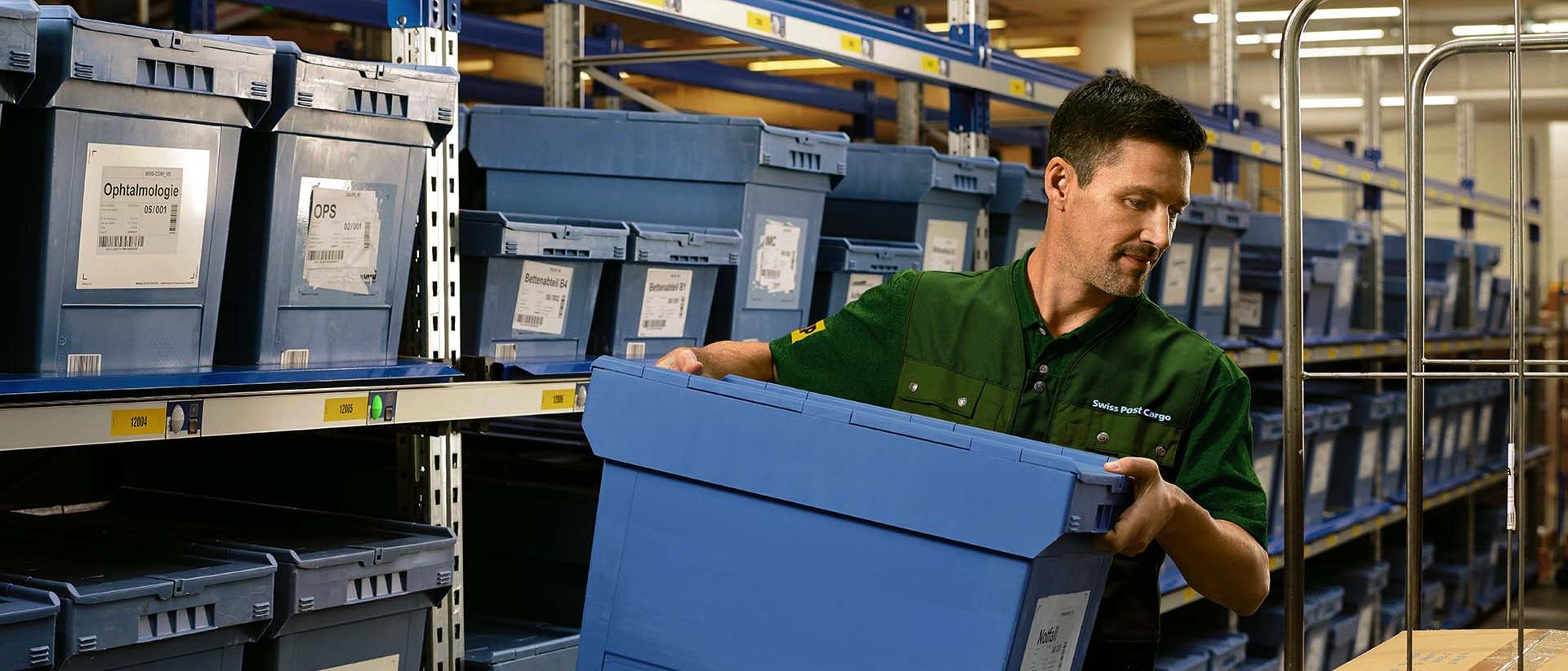 Un employé d'entrepôt charge une boîte de produits pharmaceutiques d'une étagère sur un chariot.