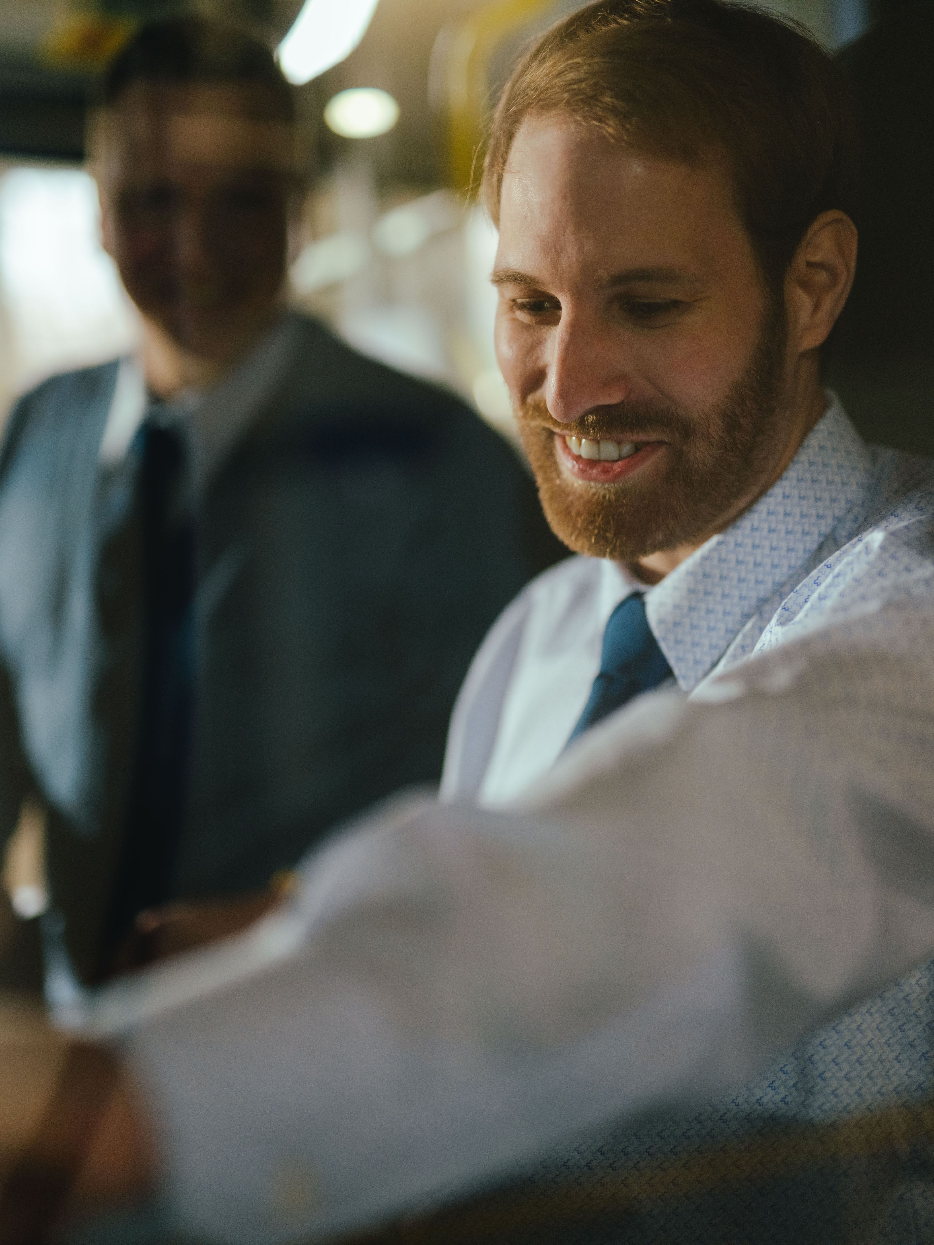 Zwei Personen befinden sich im Fahrerbereich eines Fahrzeugs. Eine Person sitzt am Steuer und greift nach einem Bedienelement, während die andere Person daneben steht. Sichtbar sind Teile des Lenkrads, der Armaturen und der Innenraumbeleuchtung.