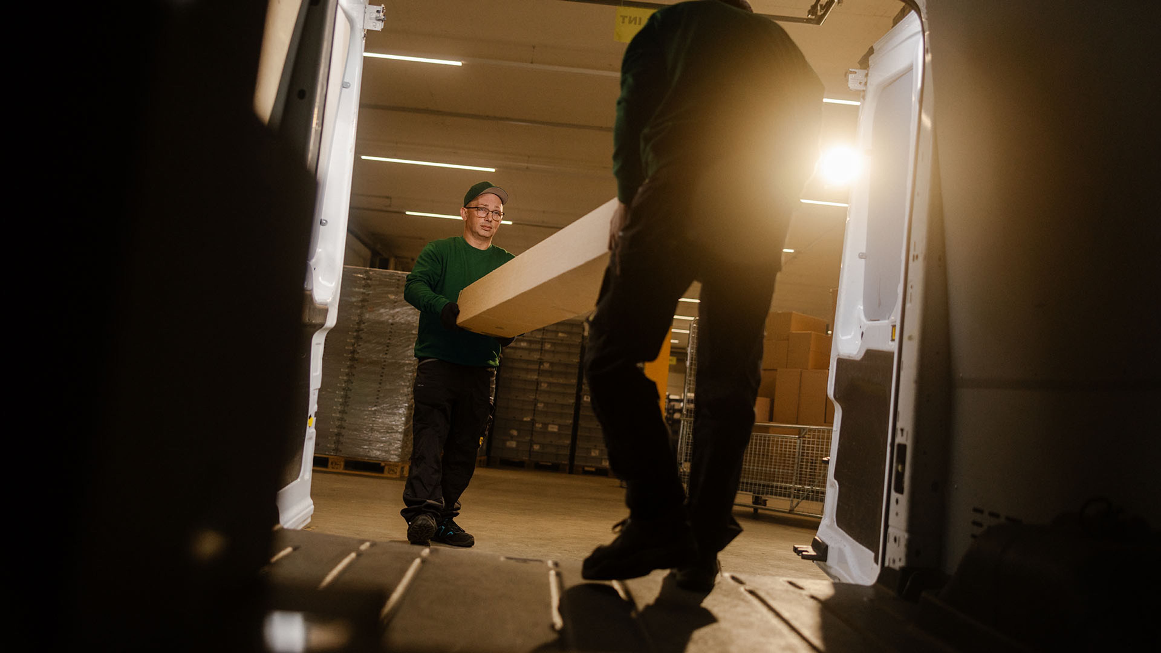 Two employees of Swiss Post Cargo load spare parts into a service vehicle at night.