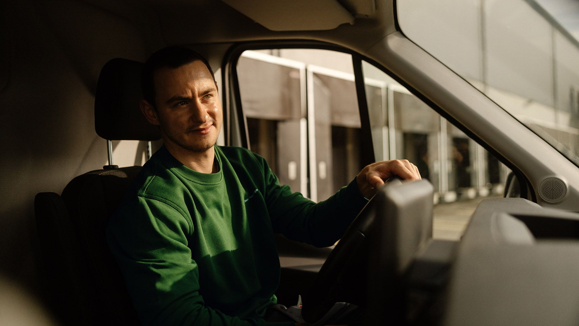 The driver of a delivery van sits behind the steering wheel, looking forward with concentration, ready for the transport order.