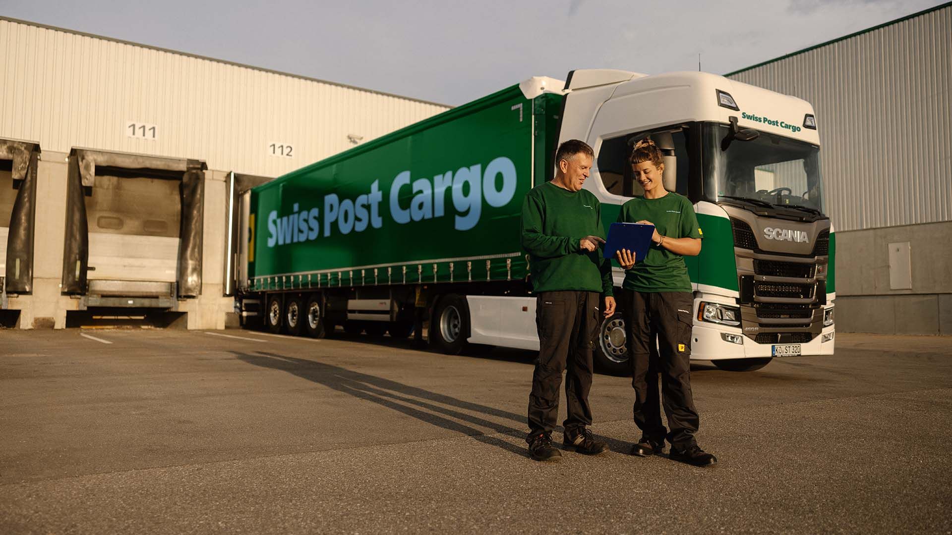 Two Swiss Post Cargo employees stand in front of a Swiss Post Cargo lorry.