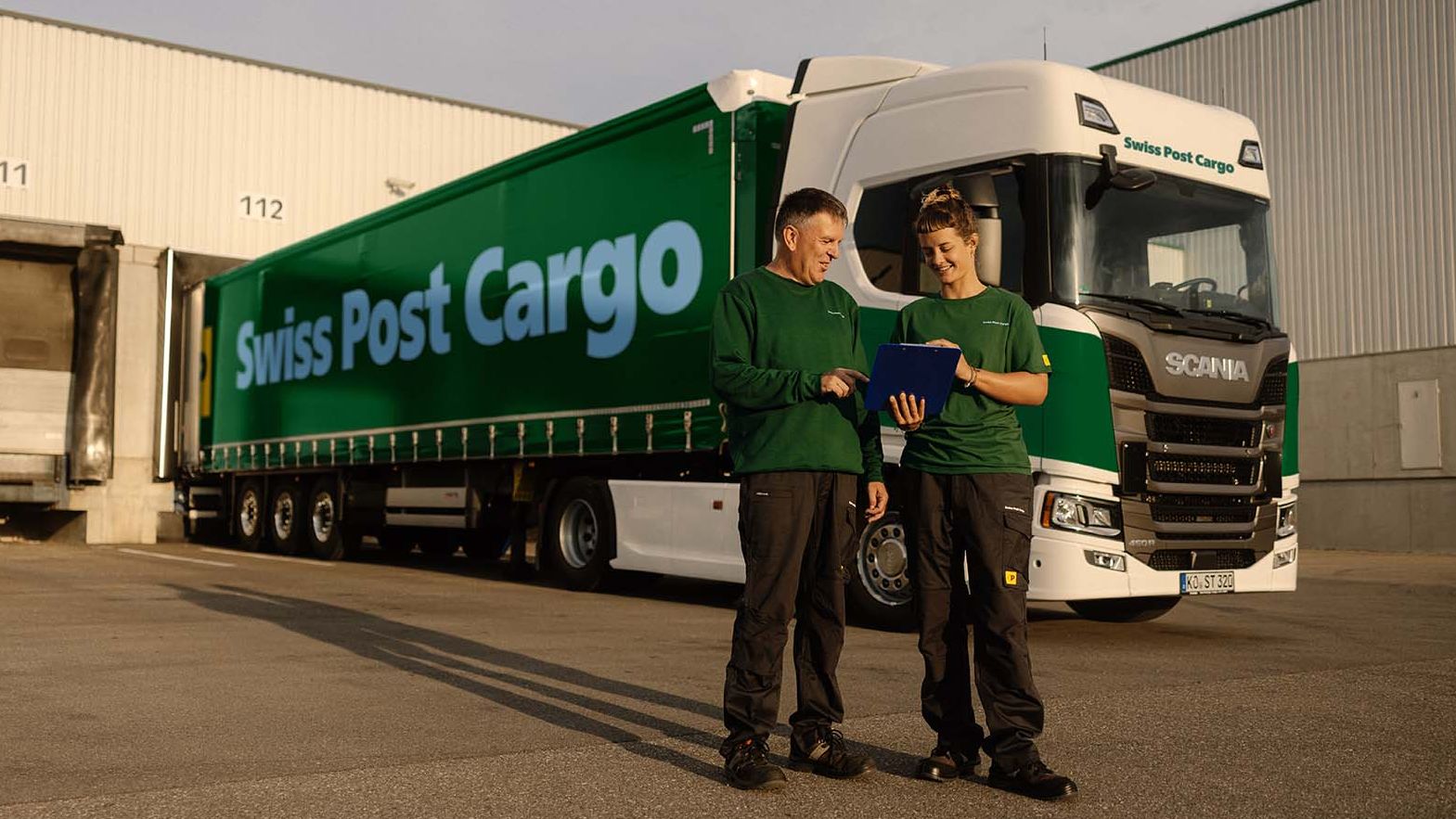Two Swiss Post Cargo employees stand in front of a Swiss Post Cargo lorry.