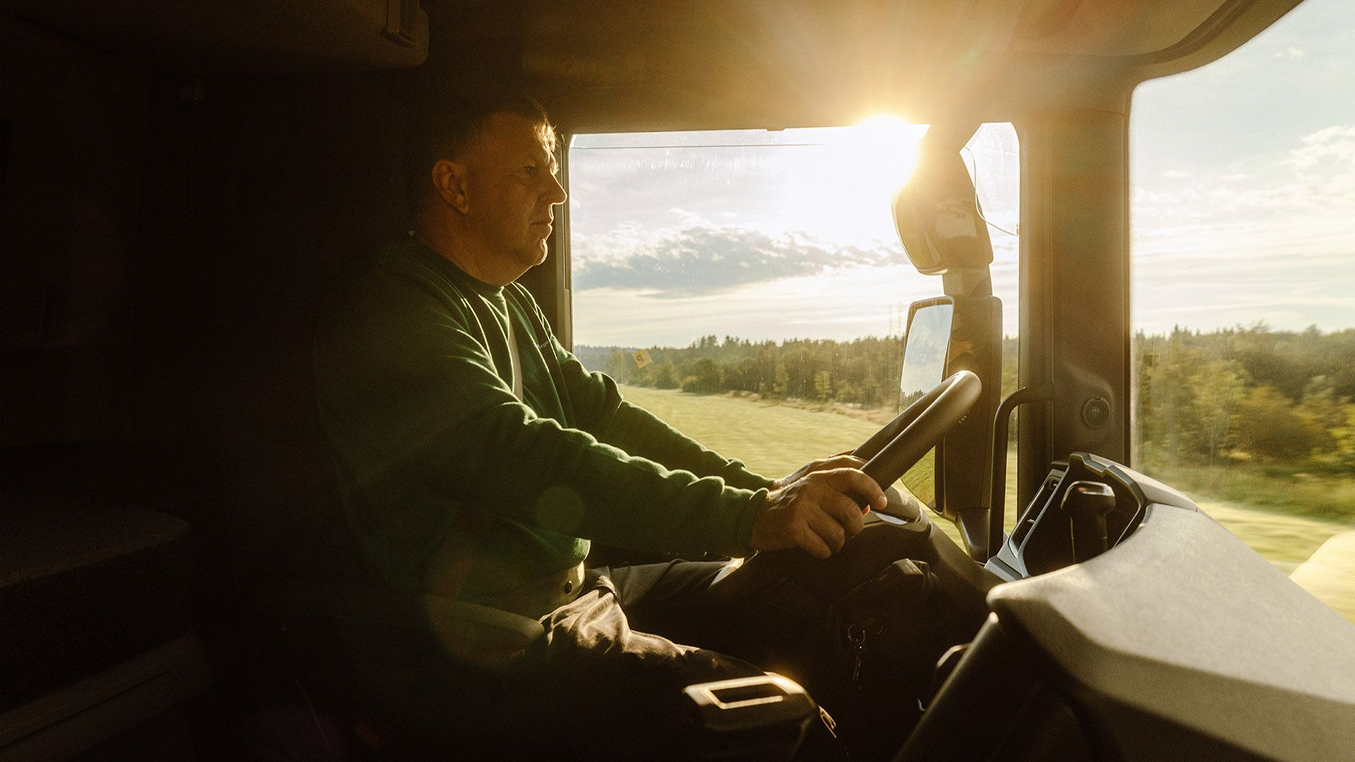 The driver of a delivery van sits behind the steering wheel, looking forward with concentration, ready for the transport order.