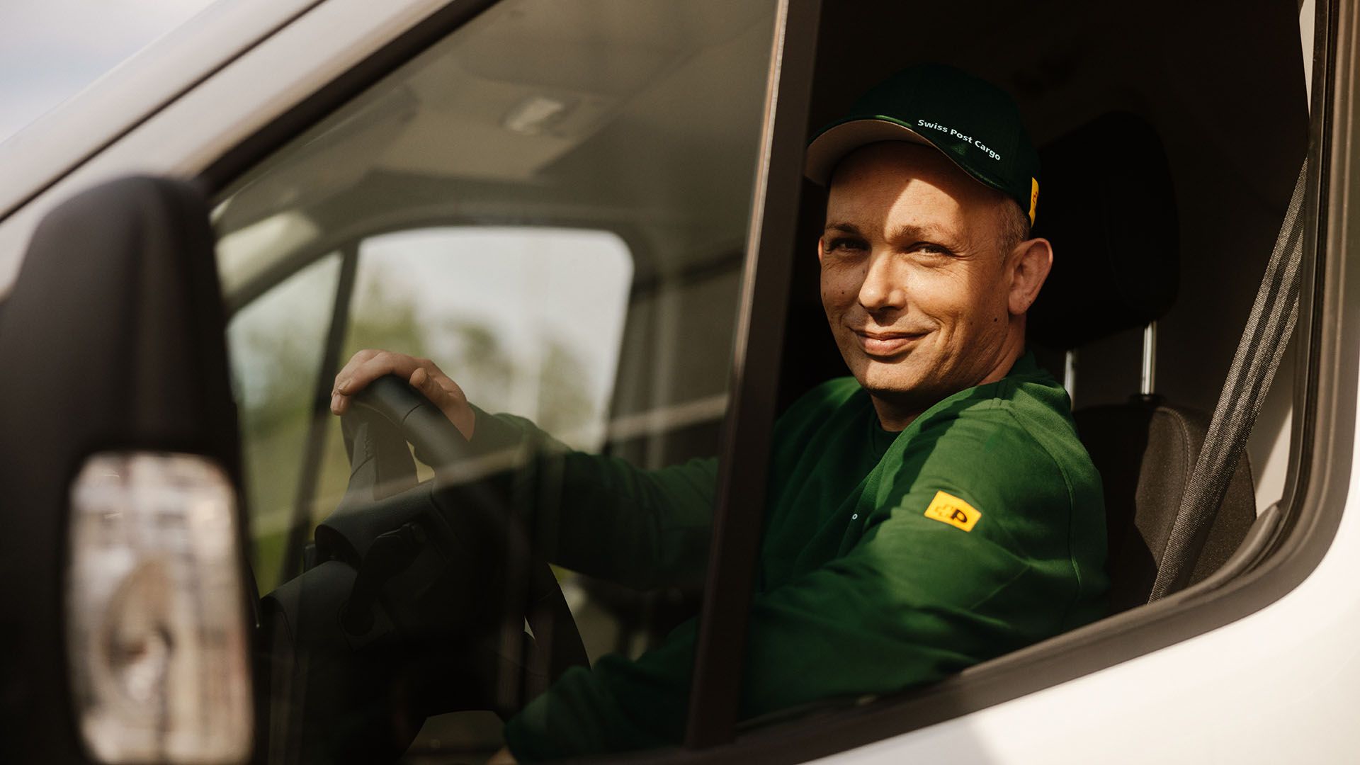 Un chauffeur de Swiss Post Cargo conduit un véhicule de livraison avec des envois de courrier de jour.