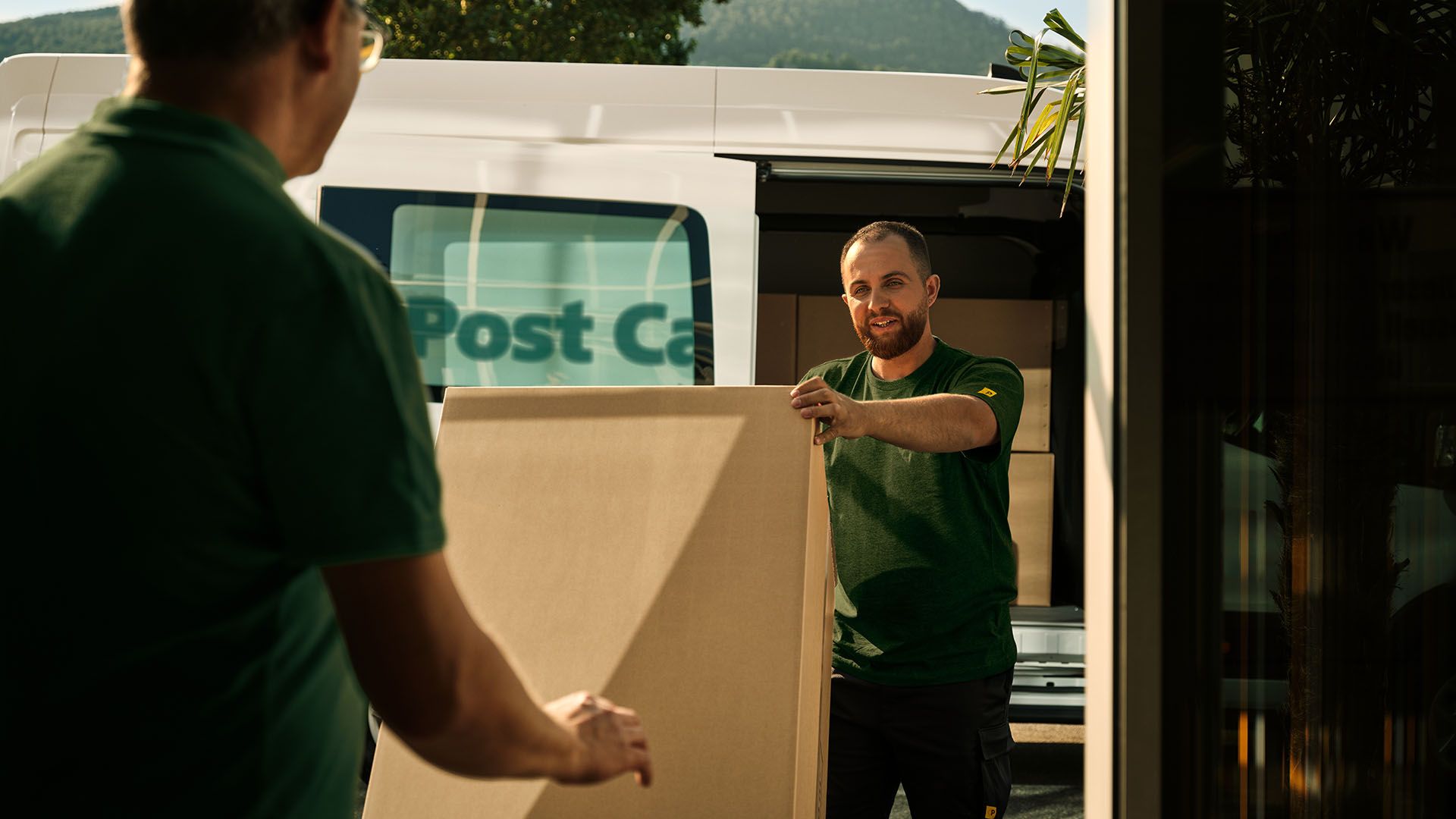 Zwei Swiss Post Cargo Mitarbeitende laden eine sperrige Lieferung aus einem Fahrzeug aus.