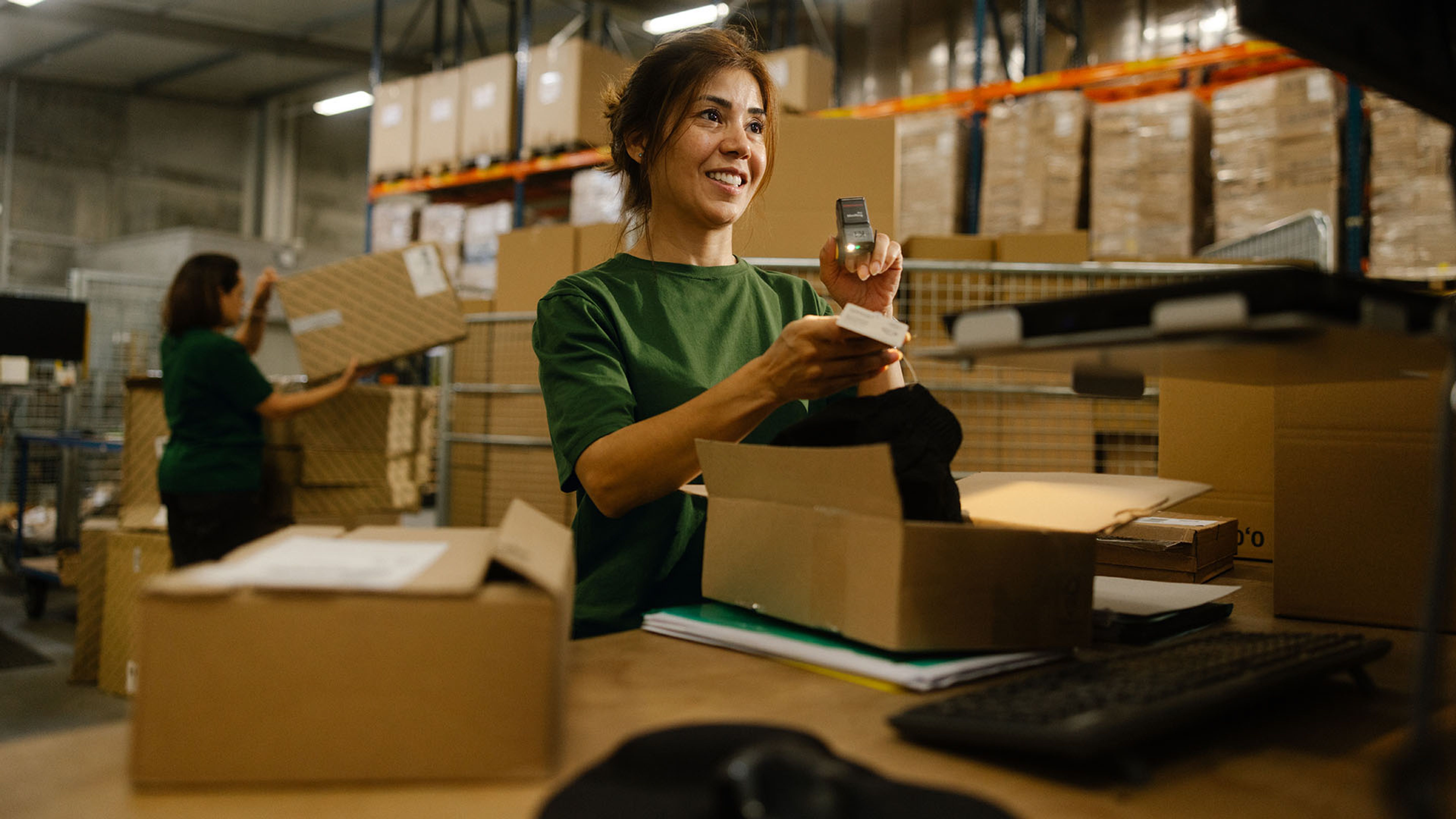 Une employée de Swiss Post Cargo vérifie le contenu d'un colis retourné. En arrière-plan, une autre employée charge un colis sur un chariot.