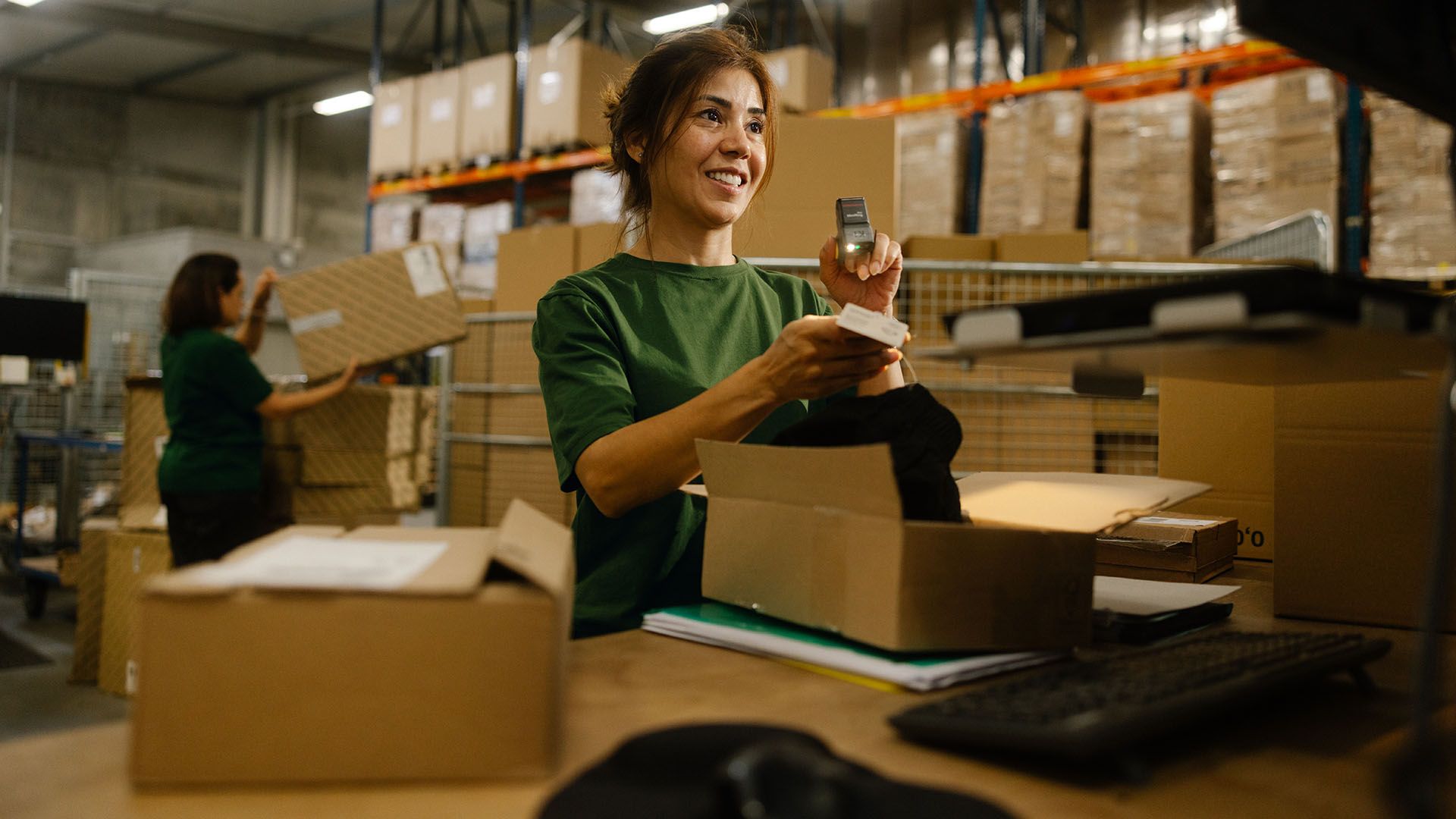 Une employée de Swiss Post Cargo vérifie le contenu d'un colis retourné. En arrière-plan, une autre employée charge un colis sur un chariot.