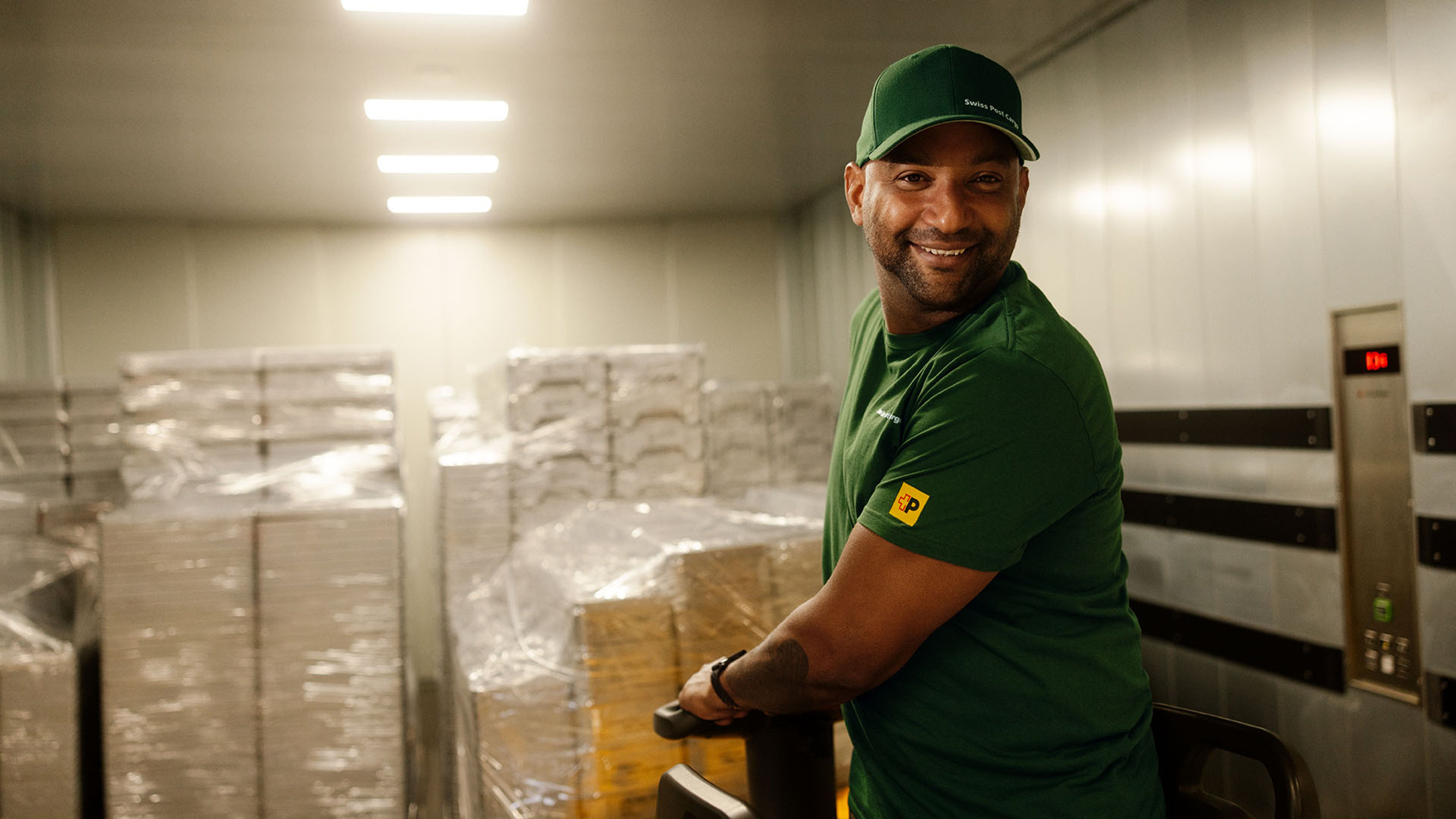 A Swiss Post Cargo warehouse worker moves general cargo on a pallet jack into an elevator.