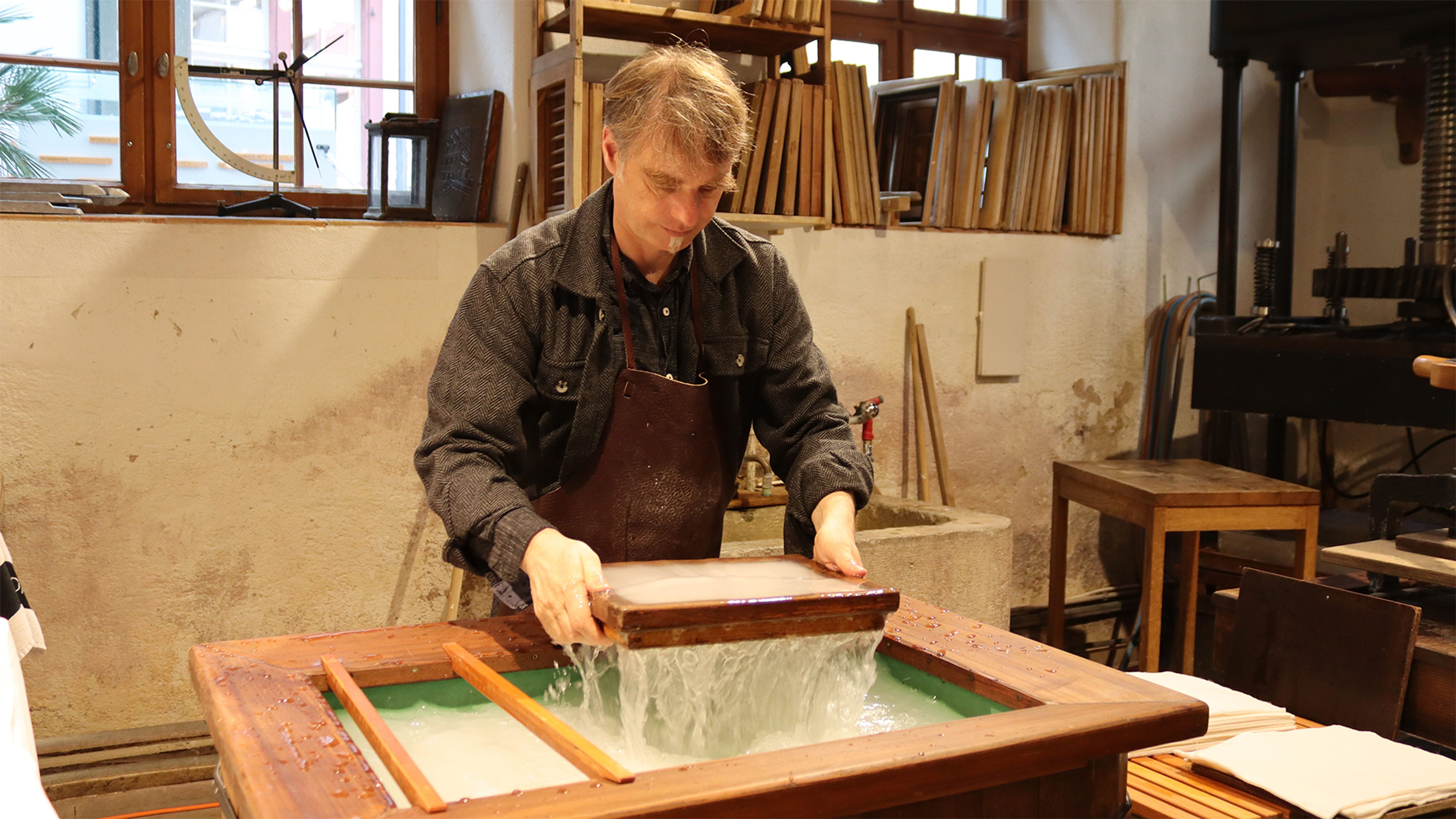 Eine Person steht in einer Werkstatt und arbeitet an einem Wasserbecken mit einem Holzrahmen.