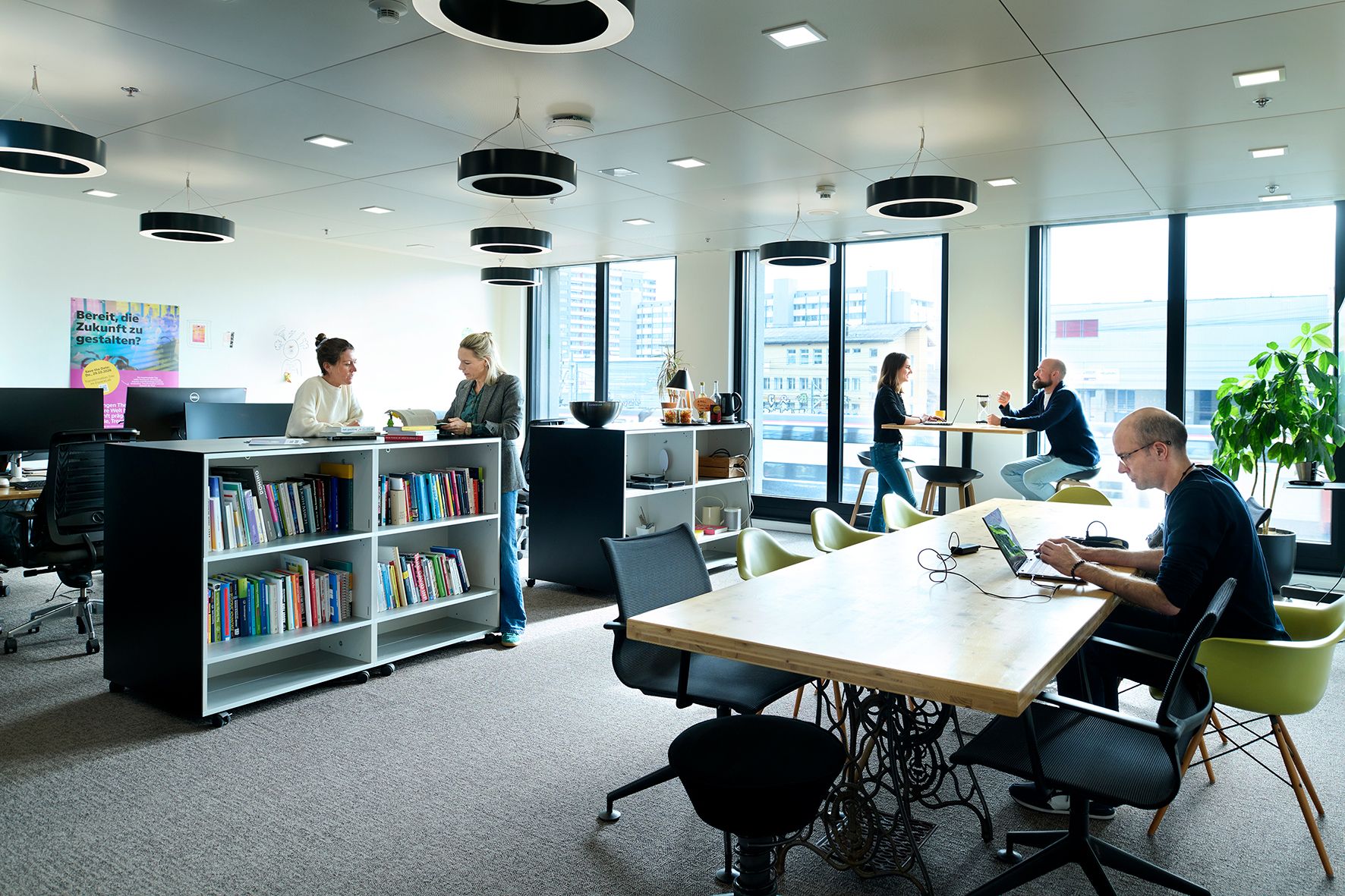 Mehrere Personen arbeiten in einem modernen, hellen Büro mit grossen Fenstern und Büchern.