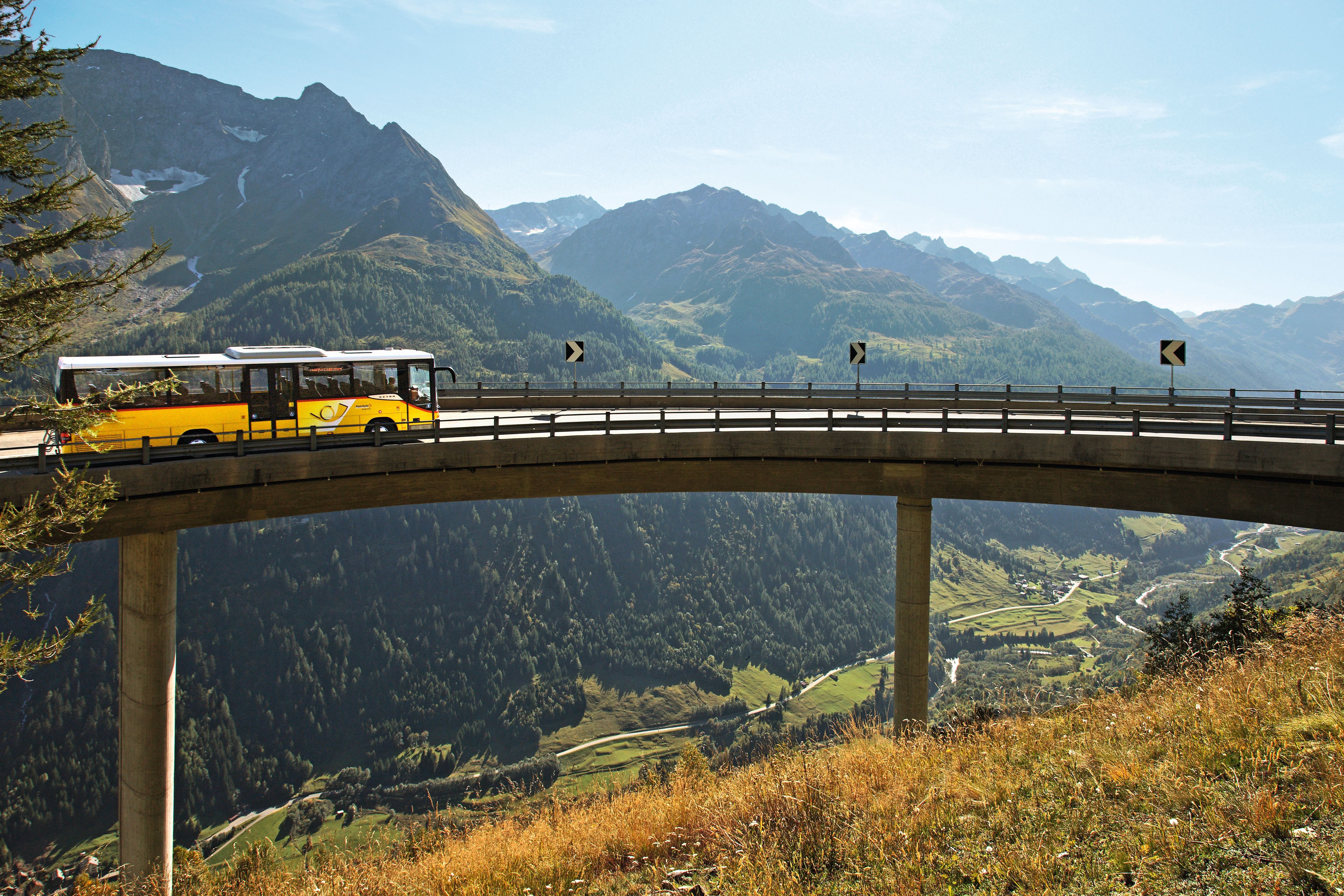 Gelber Postbus auf Brücke in den Alpen mit Bergen und Tal im Hintergrund