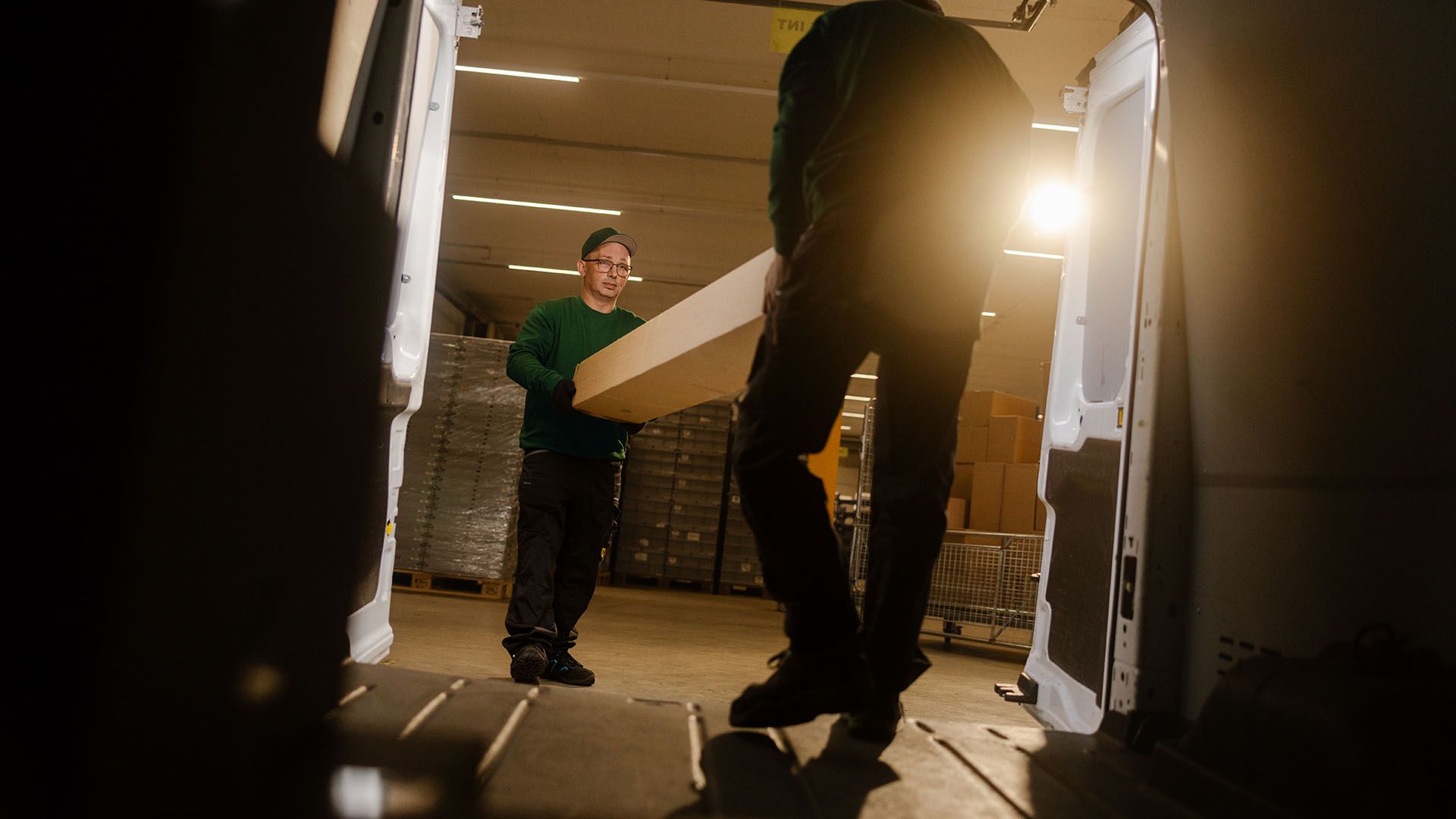 Deux employés de Swiss Post Cargo chargent des pièces de rechange dans un véhicule de service pendant la nuit.
