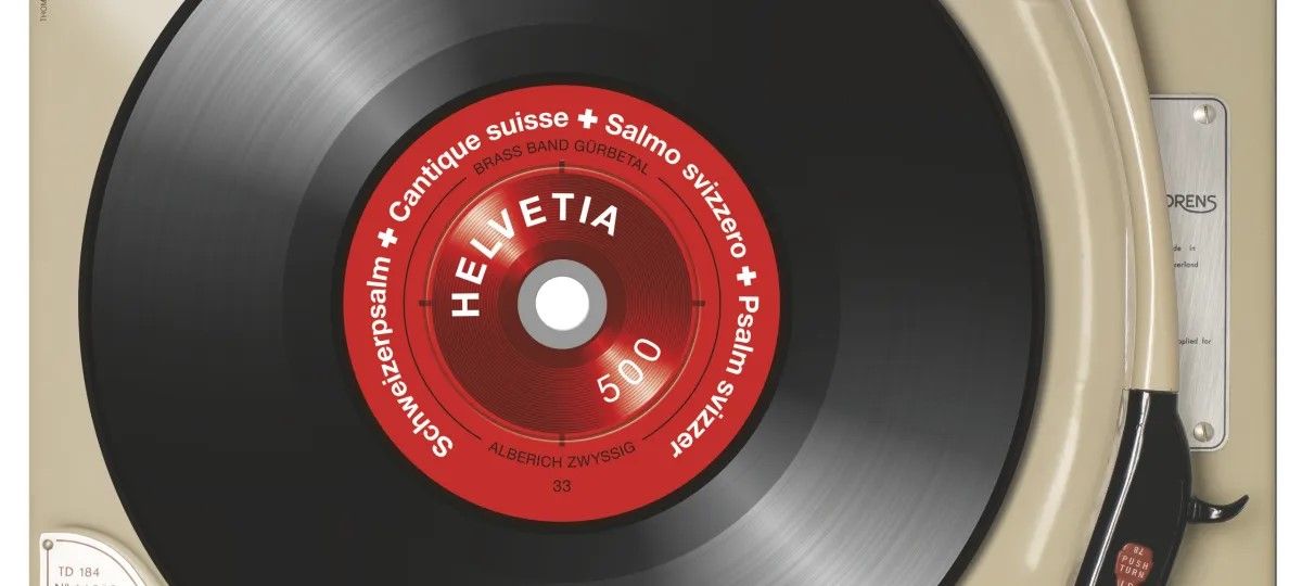 Timbre suisse représentant un disque vinyle noir sur une platine. Au centre, une étiquette rouge avec l’inscription ‘Helvetia 500’ et le texte : ‘Schweizerpsalm – Cantique suisse – Salmo svizzero – Psalm svizzer’.