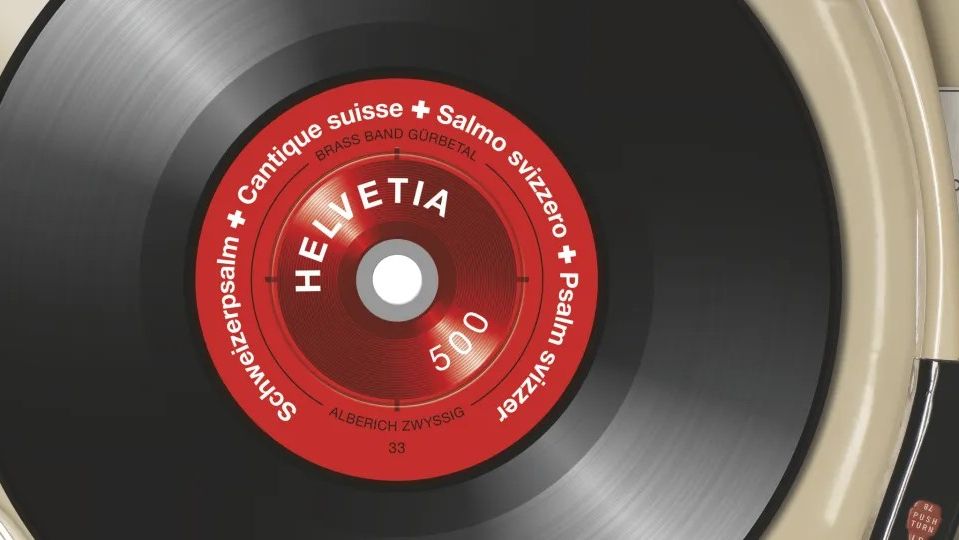 Timbre suisse représentant un disque vinyle noir sur une platine. Au centre, une étiquette rouge avec l’inscription ‘Helvetia 500’ et le texte : ‘Schweizerpsalm – Cantique suisse – Salmo svizzero – Psalm svizzer’.