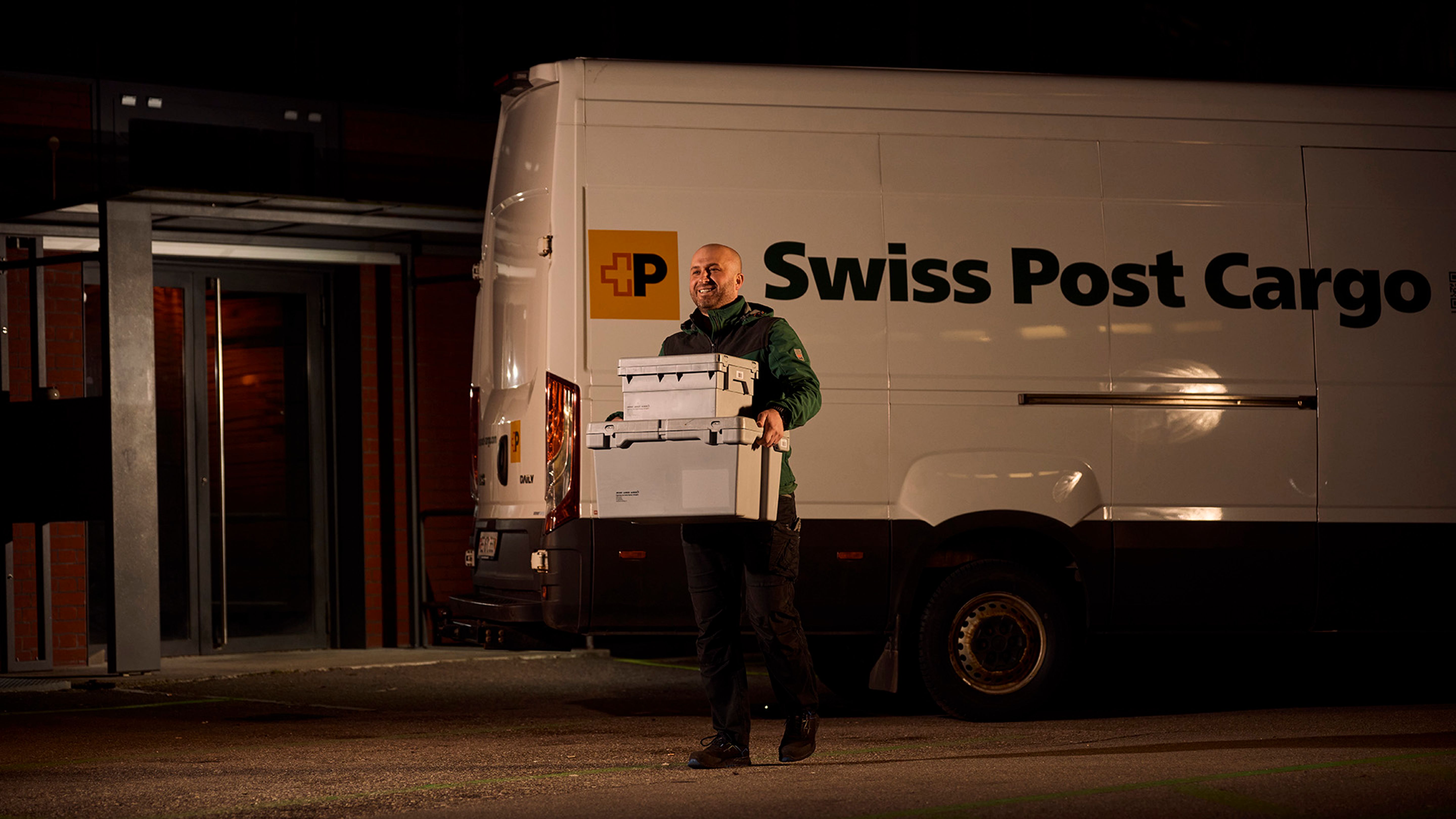 Swiss Post Cargo Mitarbeiter mit Paketen vor dem Lieferfahrzeug in der Nacht.