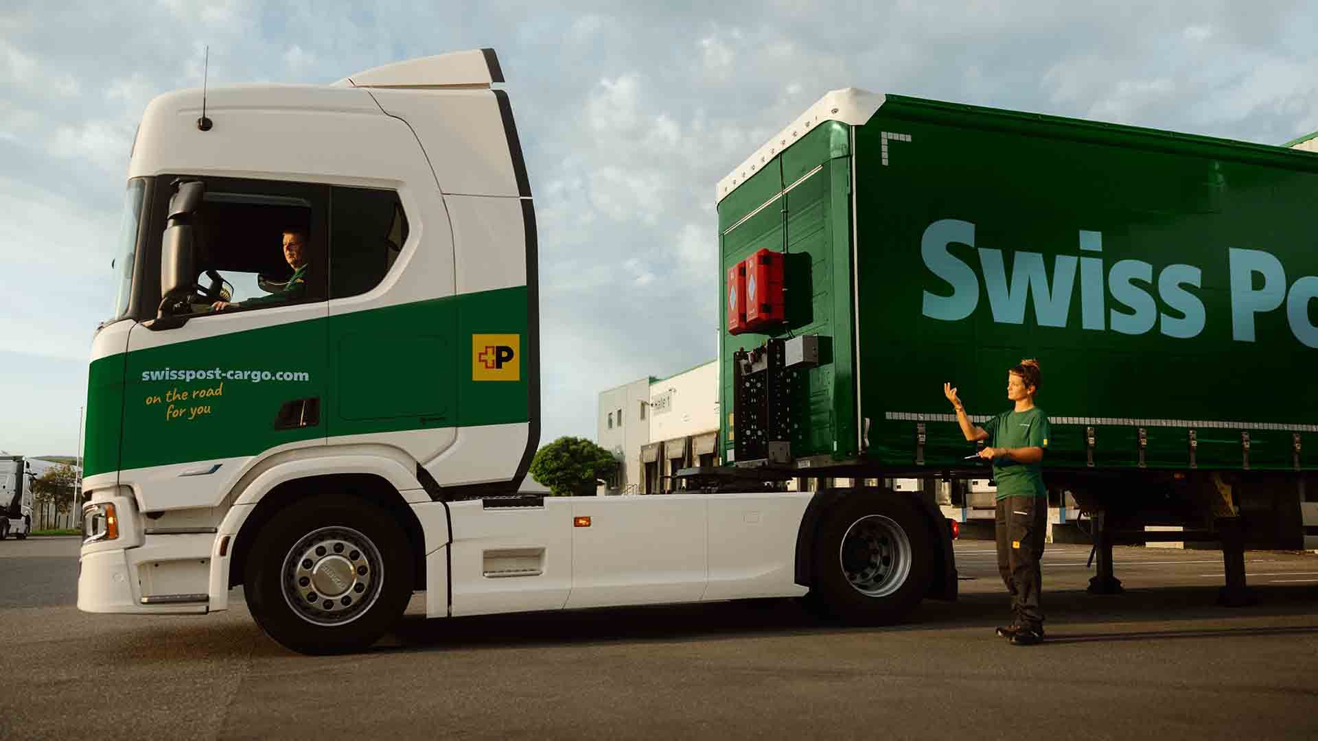 Ein Swiss Post Cargo LKW-Fahrer kuppelt mit der Hilfe einer Kollegin einen Anhänger an.