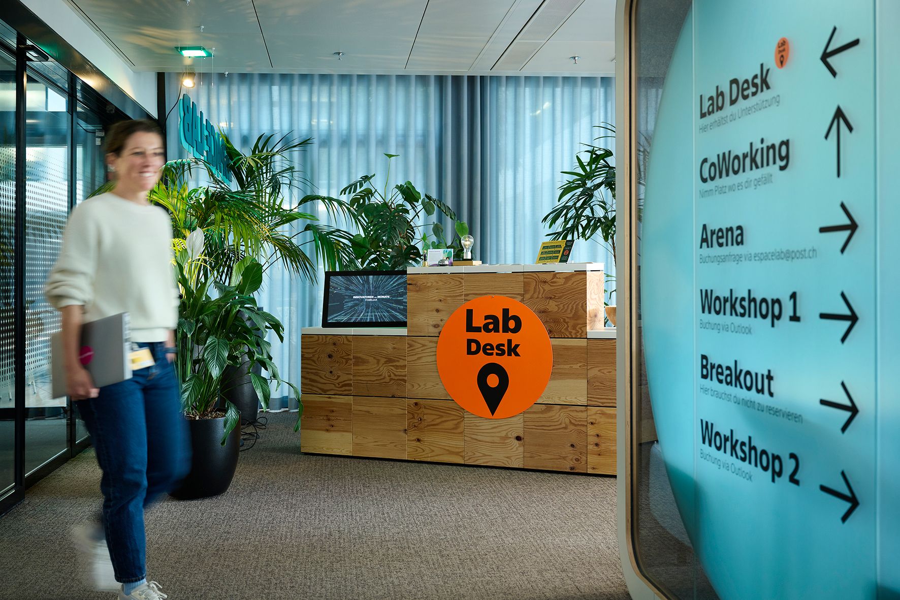Eine Person geht an einem Empfangstresen mit "Lab Desk"-Schild in einem modernen Büro vorbei.