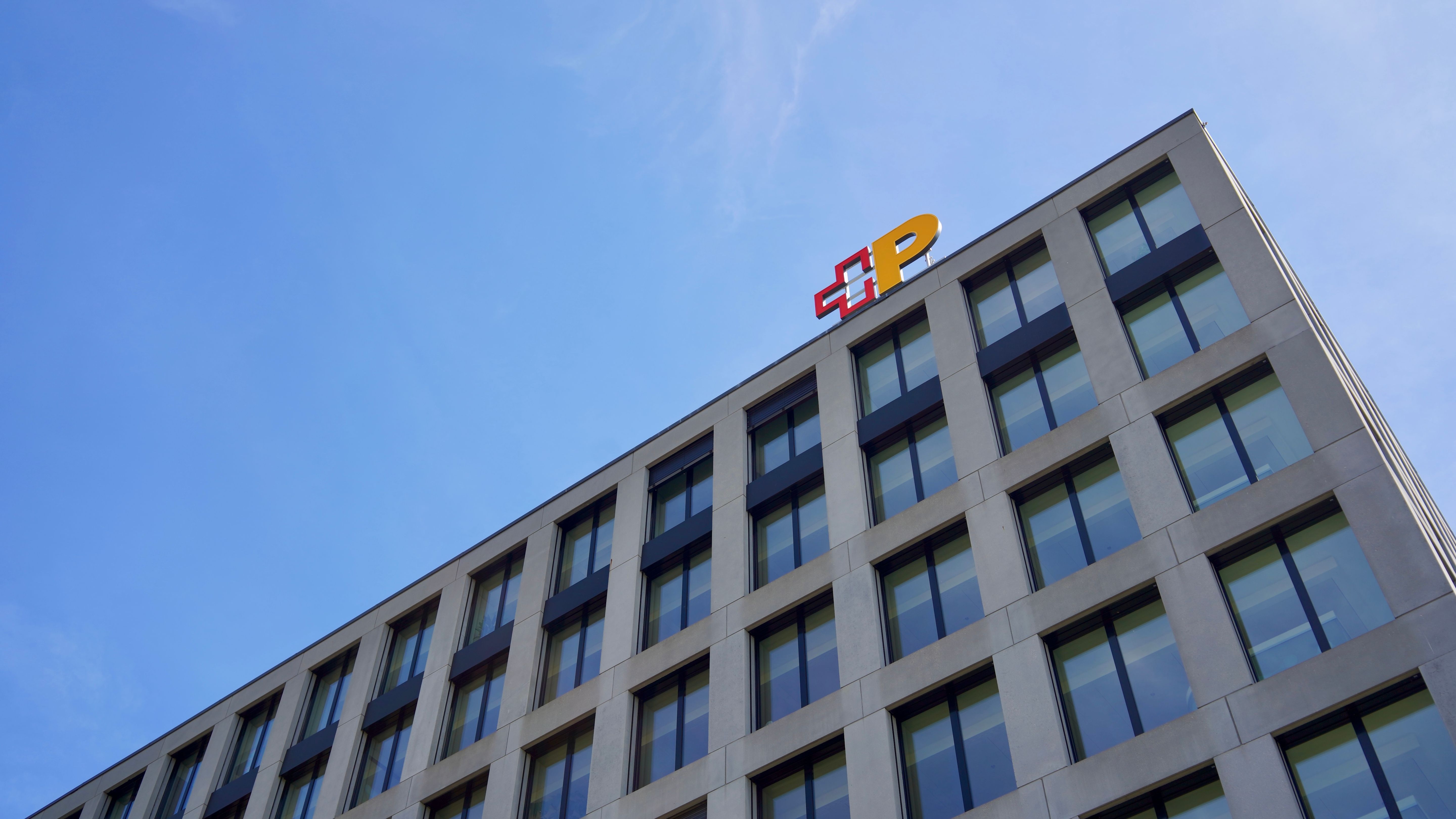 Gebäude mit Logo der Schweizerischen Post auf dem Dach vor blauem Himmel