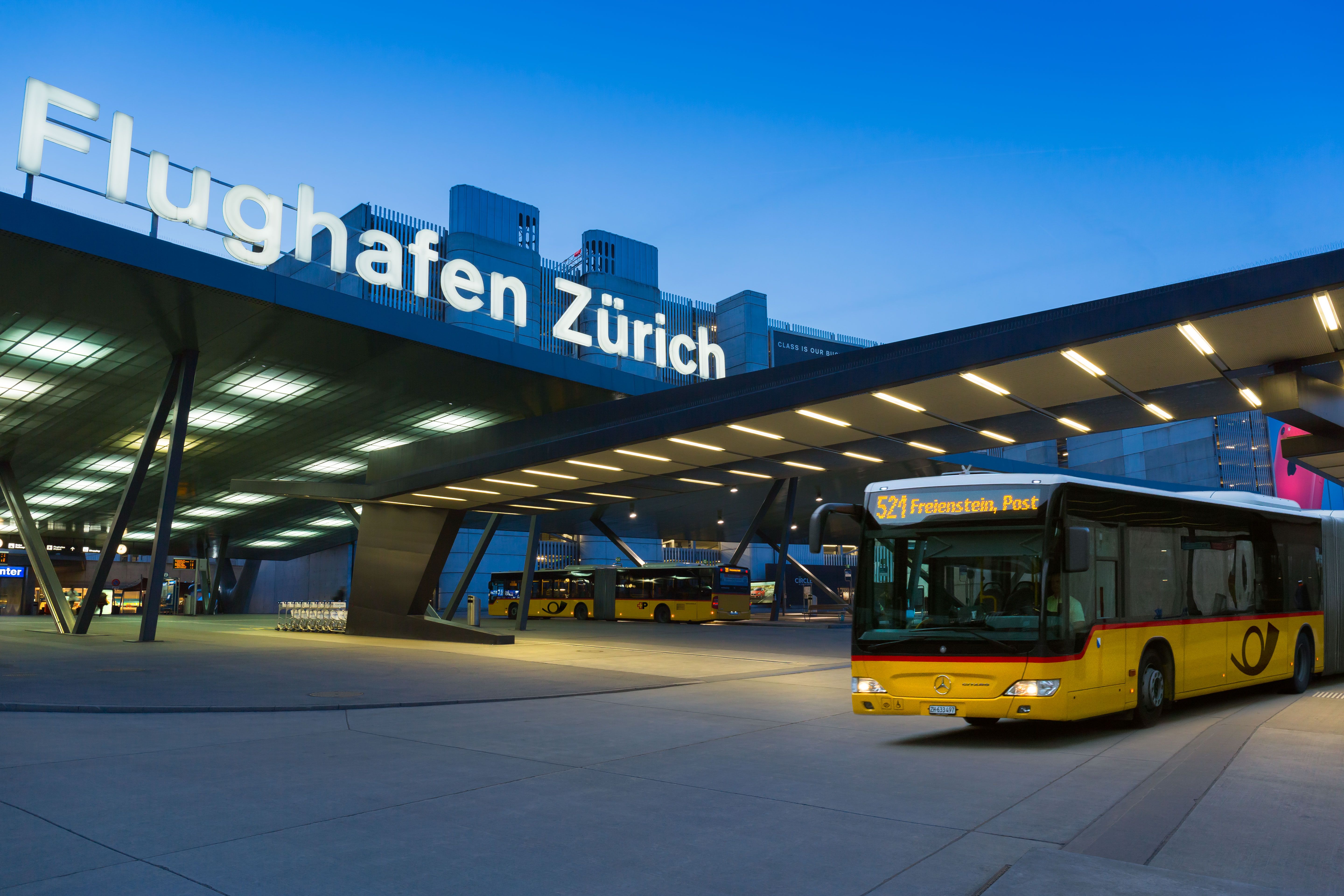 Busbahnhof am Flughafen Zürich mit gelben Postbussen bei Abendlicht