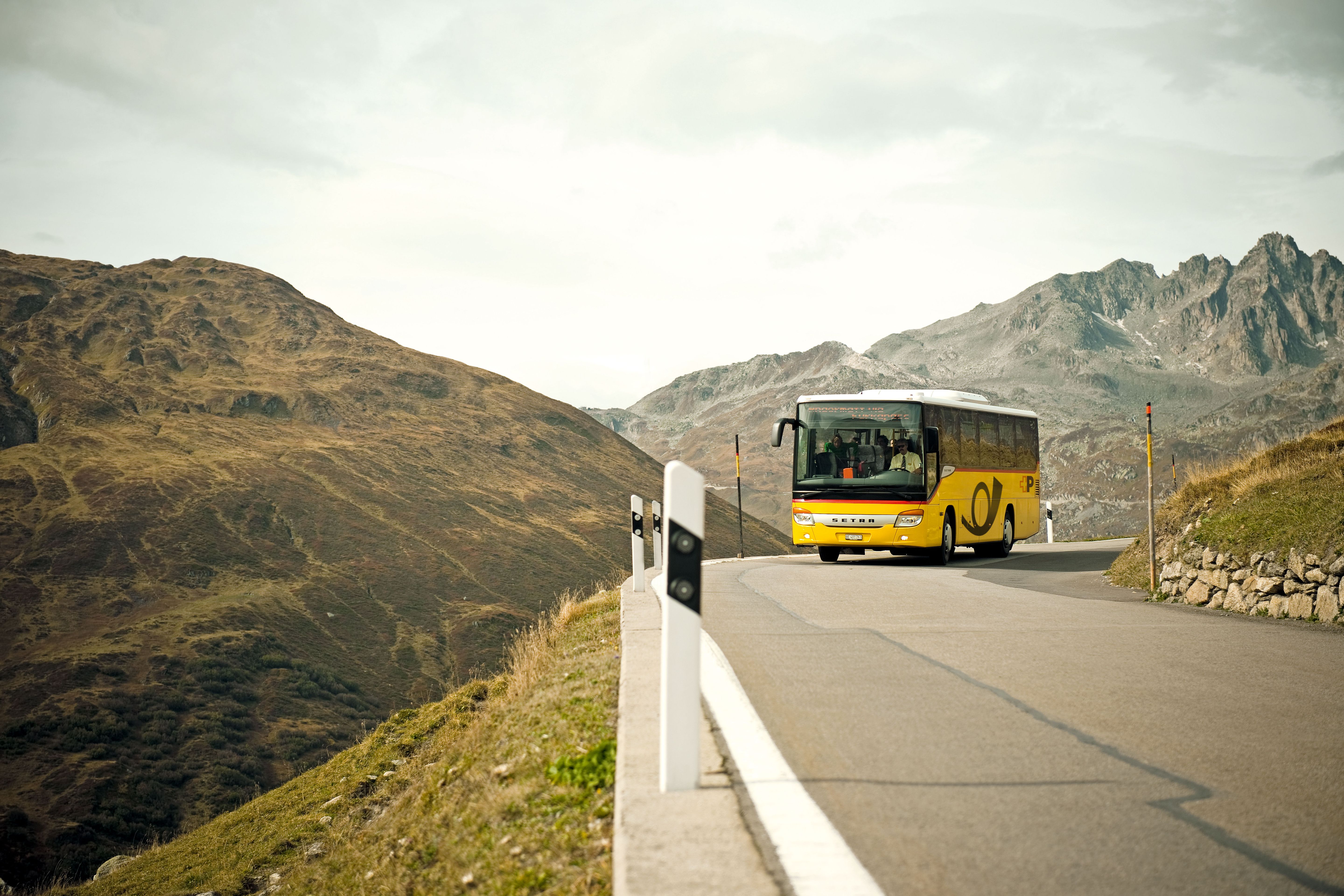 Gelber Postbus auf kurviger Bergstraße mit Bergen im Hintergrund