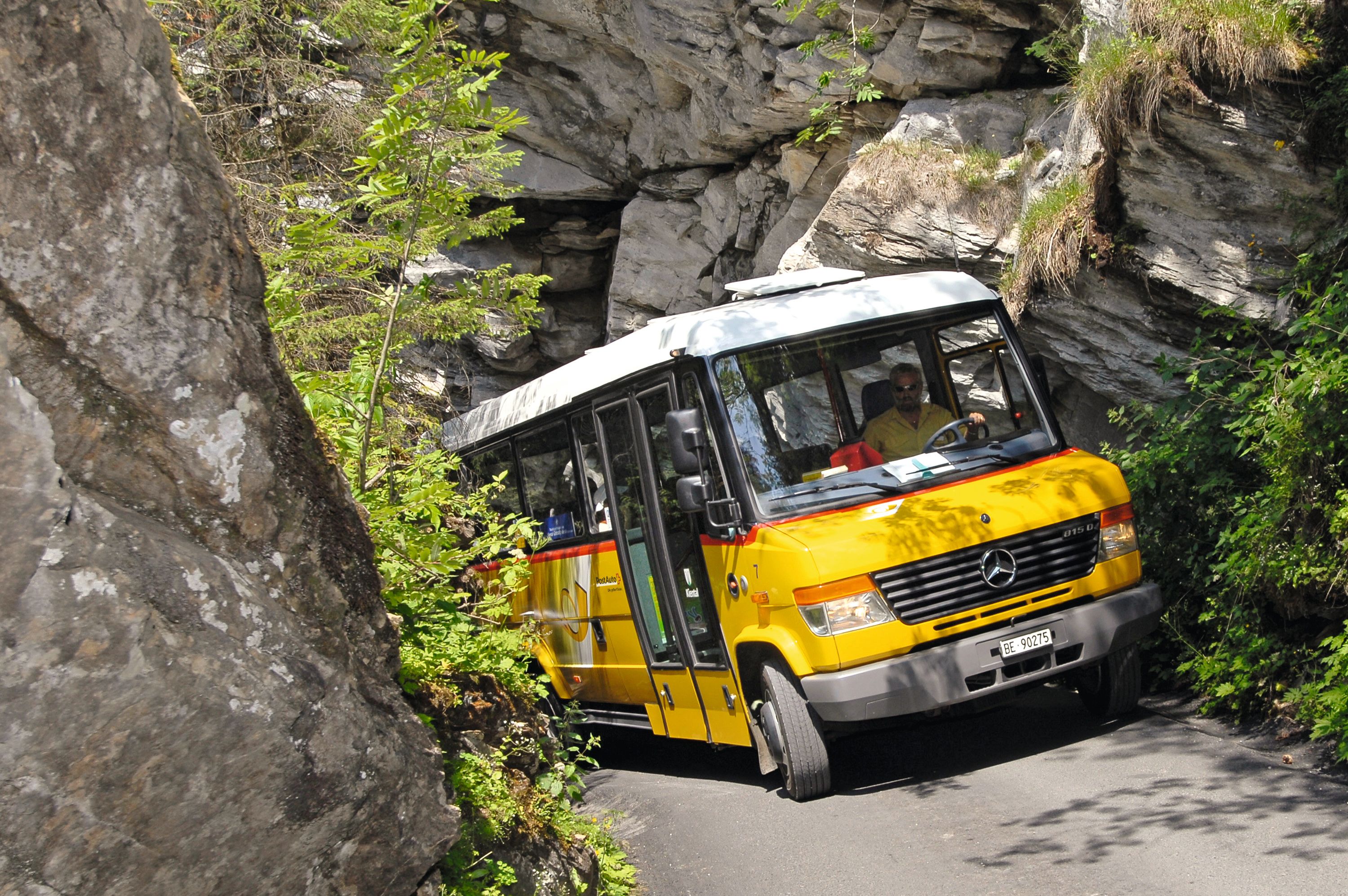 Gelber Postbus auf enger Bergstraße zwischen Felsen