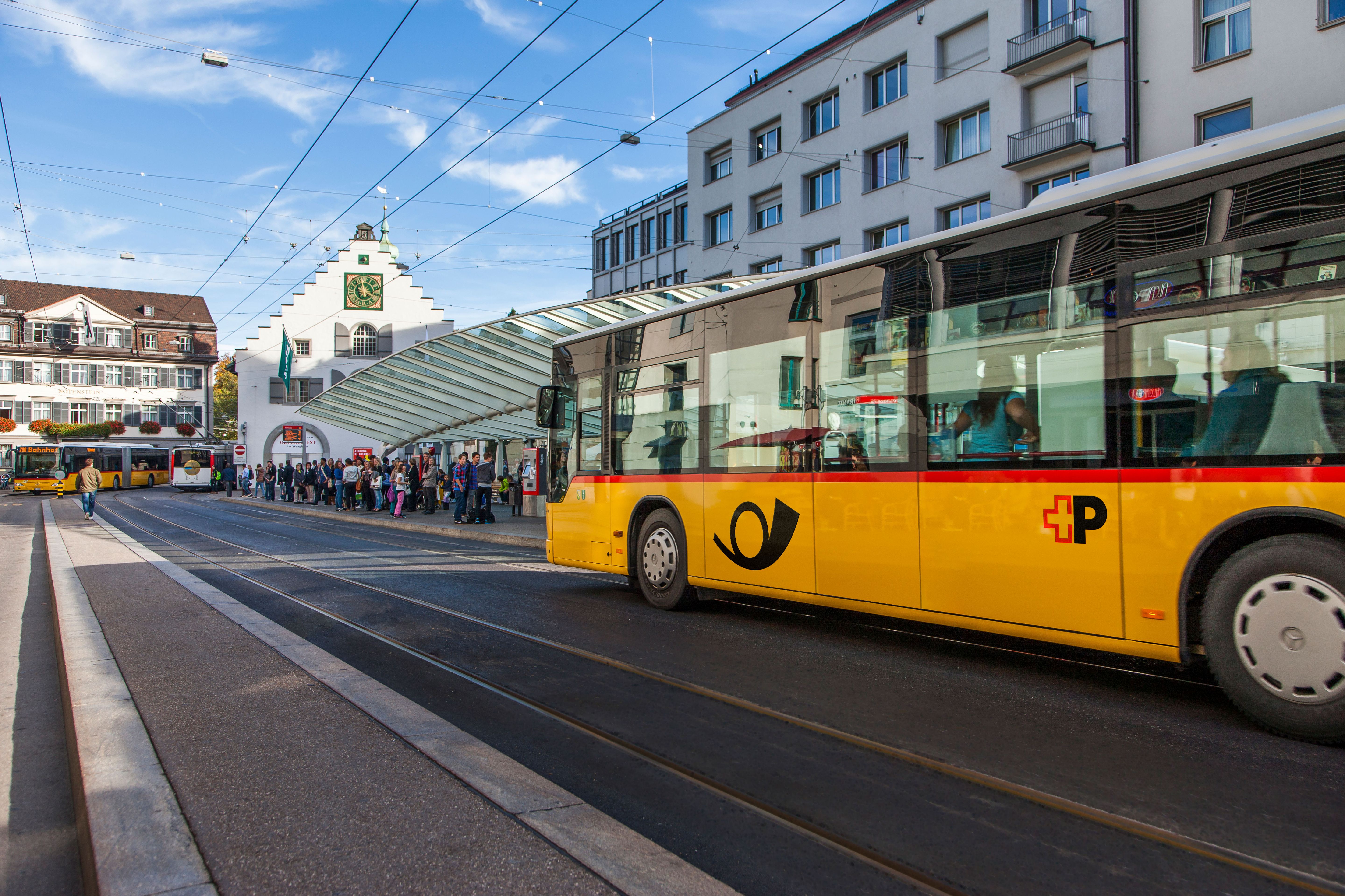 Gelber Postbus an Haltestelle vor historischem Gebäude mit Uhr
