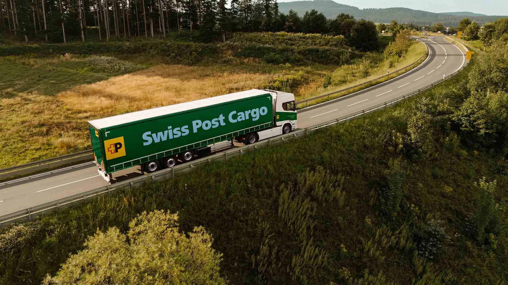 A Swiss Post Cargo truck drives on a country road, transporting goods.