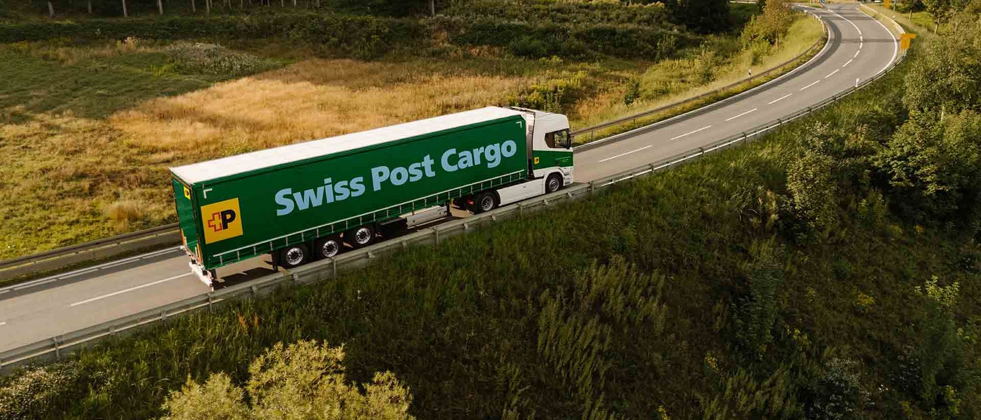 A Swiss Post Cargo truck drives on a country road, transporting goods.