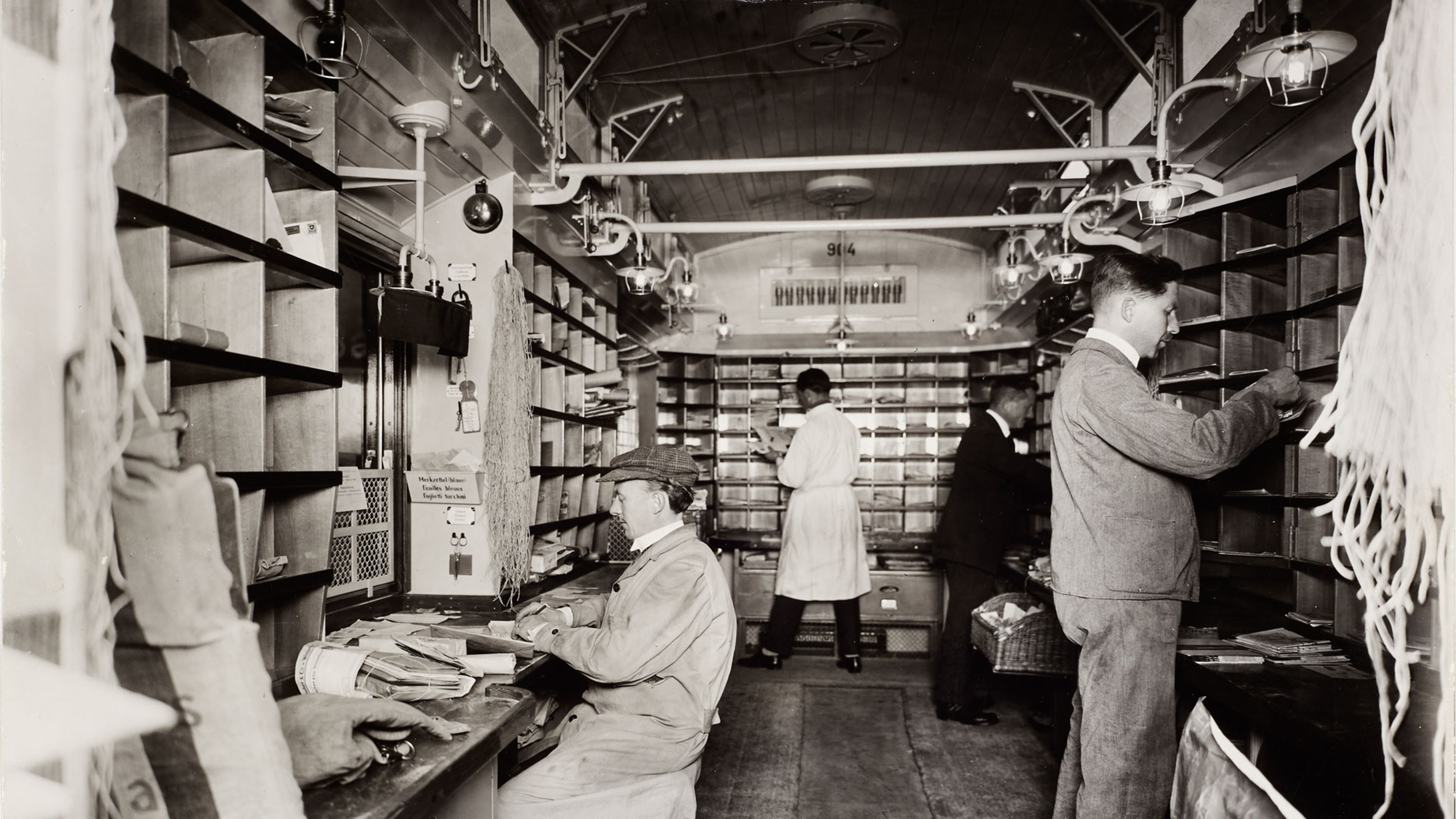 Postiers ambulants lors du tri en cours de route dans le bureau du wagon-poste sur la ligne Bâle–Belfort en 1926. Source: musée de la communication