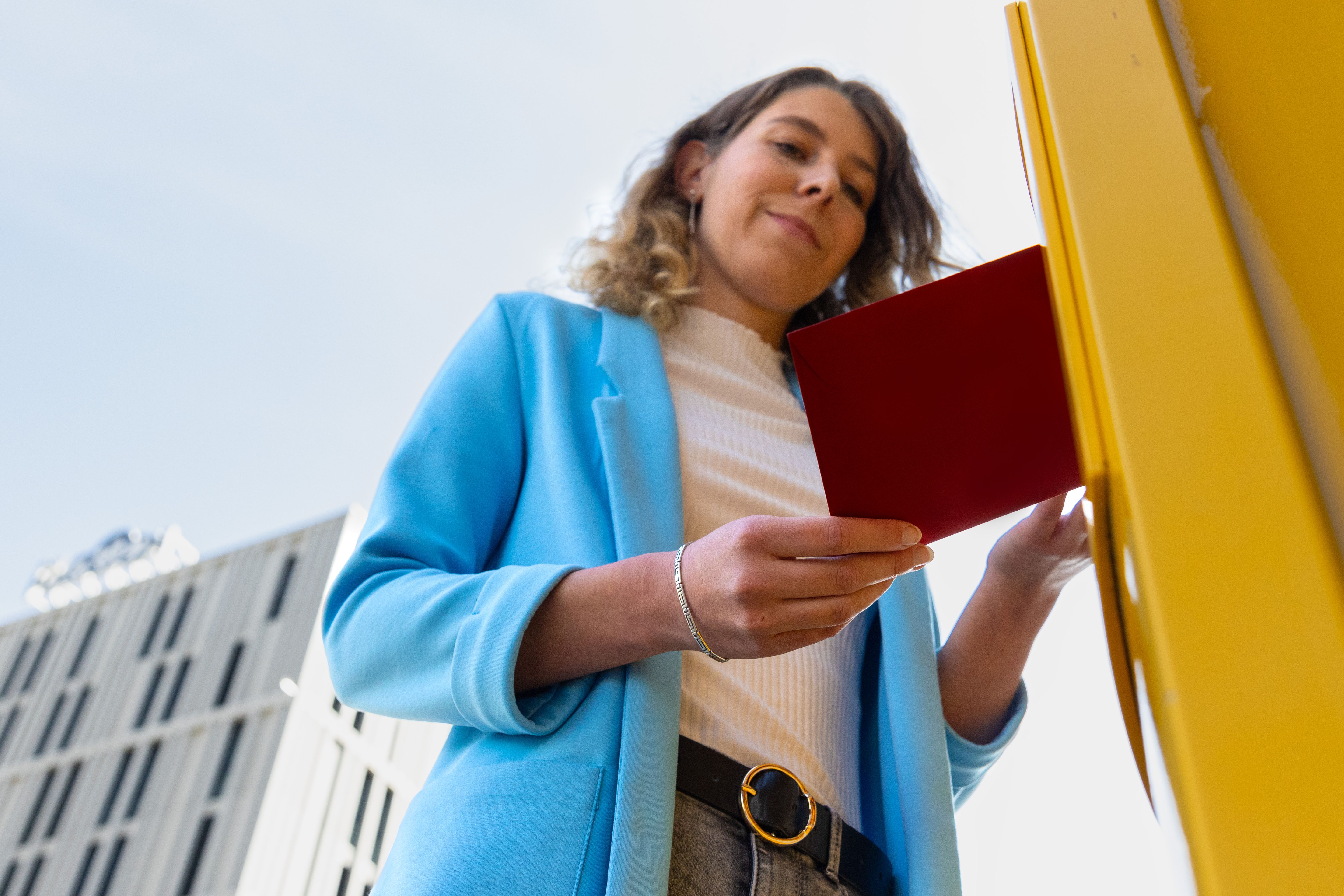 Eine Frau wirft einen roten Brief in einen Post-Briefkasten.